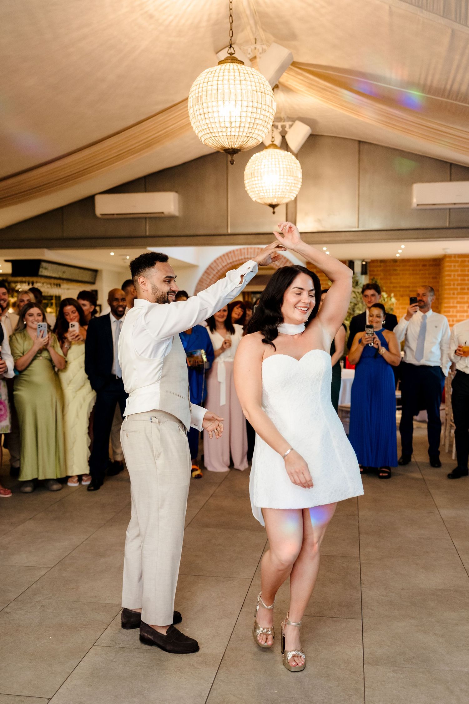 Groom spinning bride in white mini dress during first dance at wedding reception.