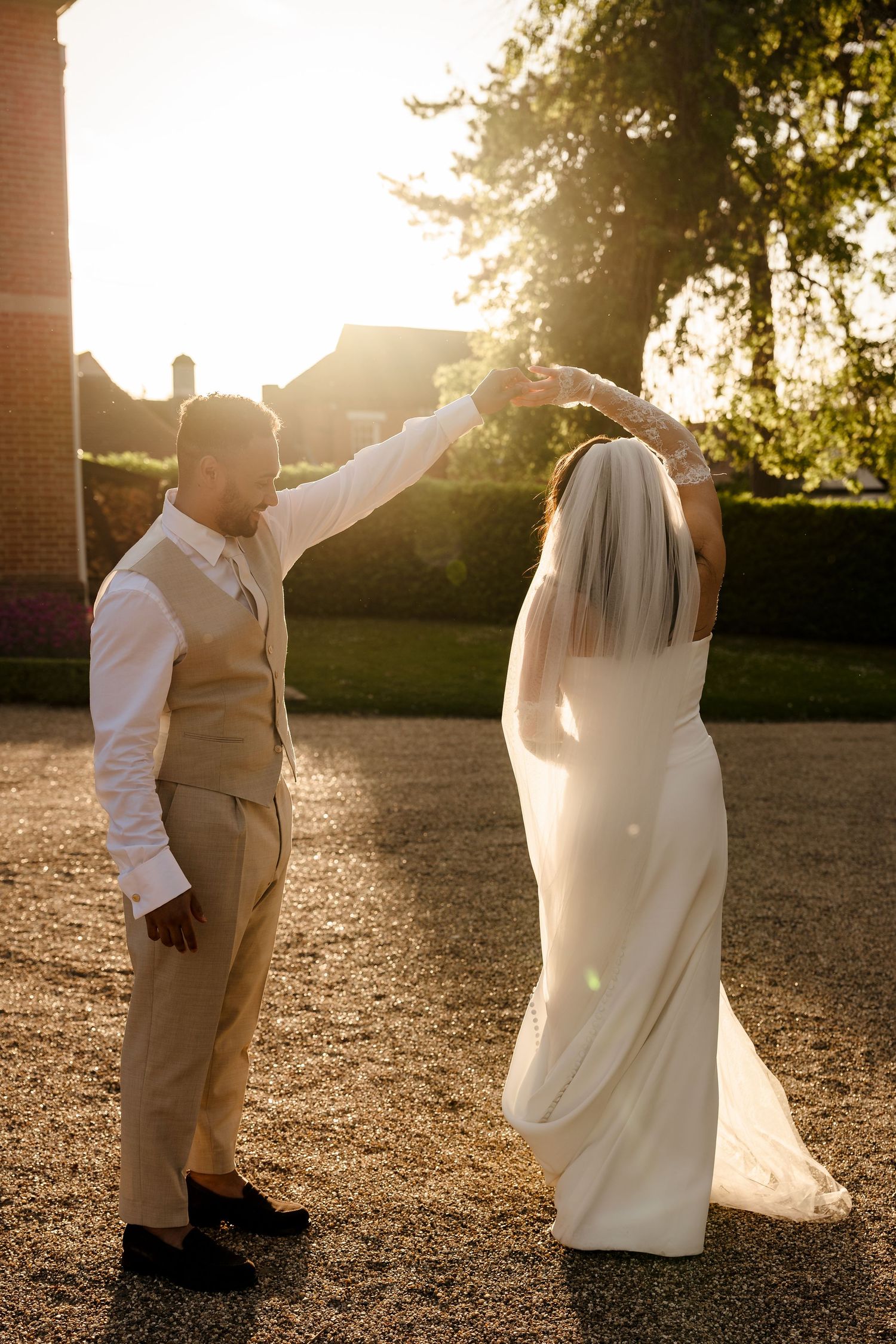 Bride and groom dancing in golden sunset light outside rustic venue, groom spinning bride in white gown.