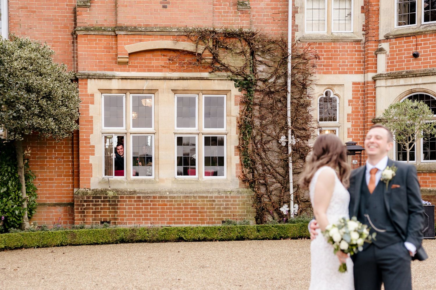Bride and groom share a joyful moment outside a grand red brick wedding venue.