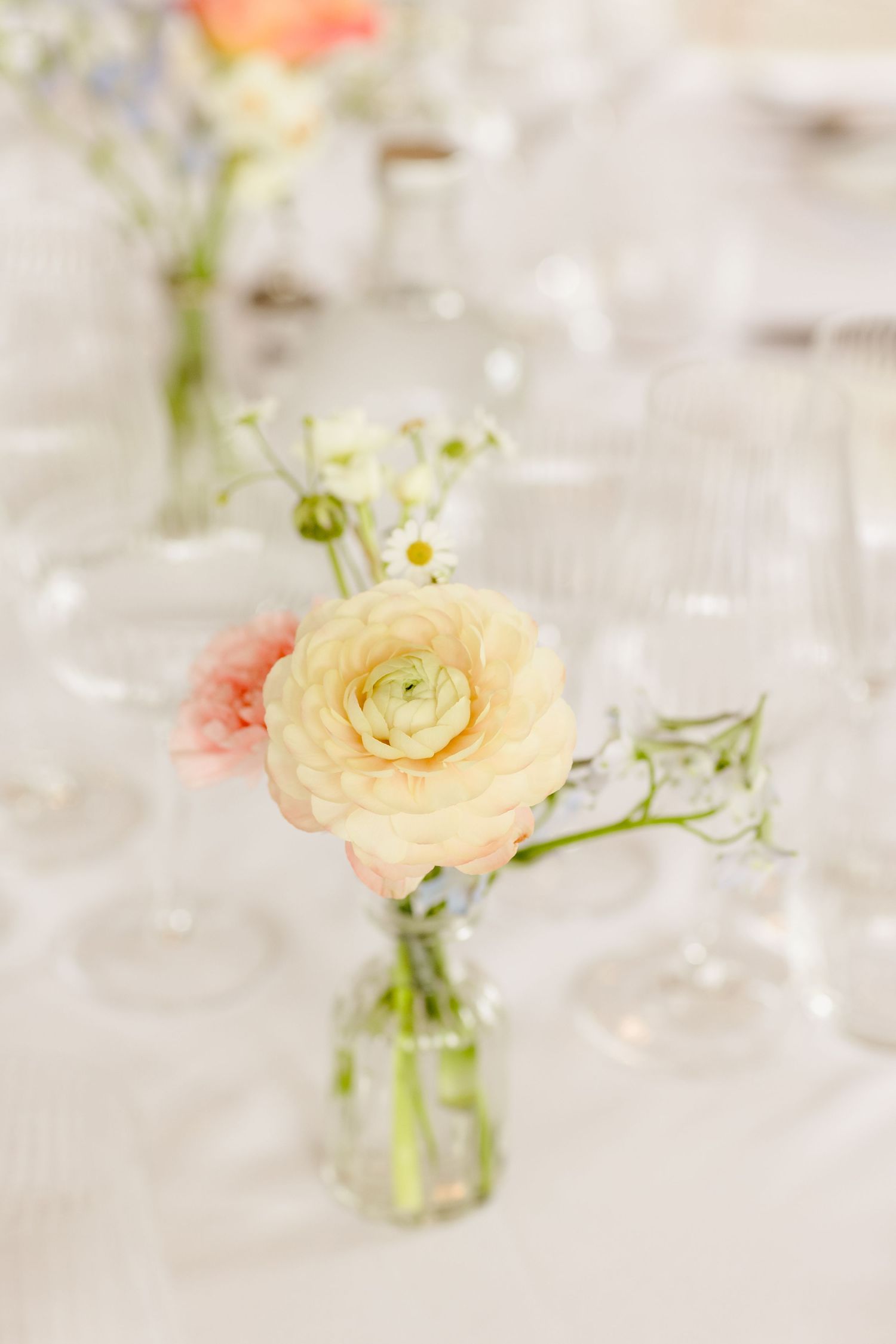 Elegant wedding table centerpiece with cream ranunculus and pink roses in glass bud vase.