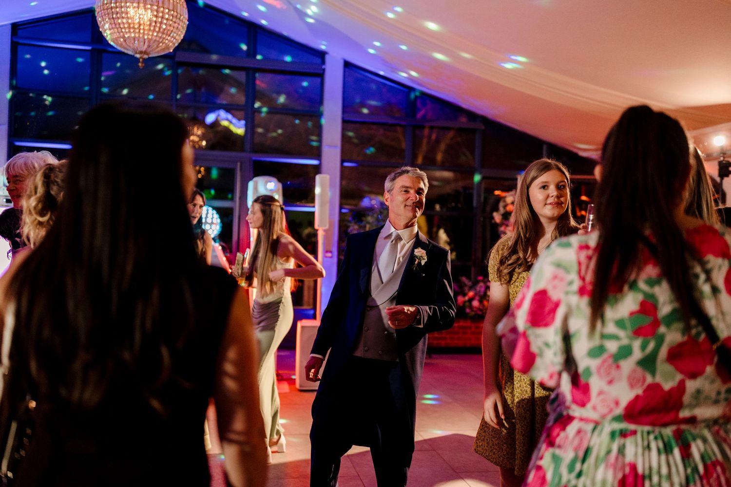 Wedding guests dancing under colorful lights at lively evening wedding reception party.
