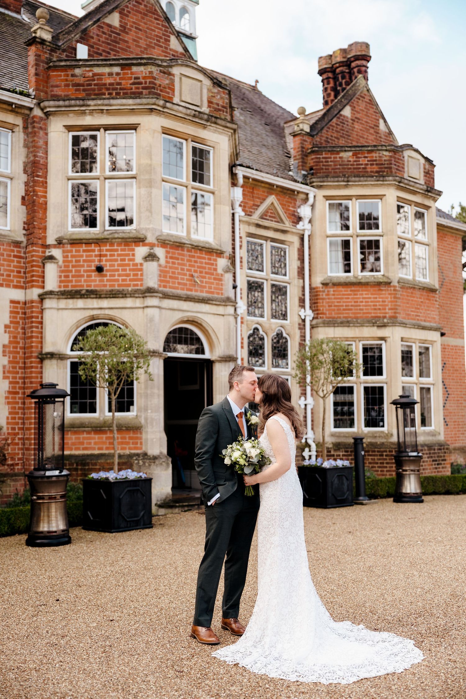 Bride and groom share a kiss outside a stunning red brick English manor wedding venue.
