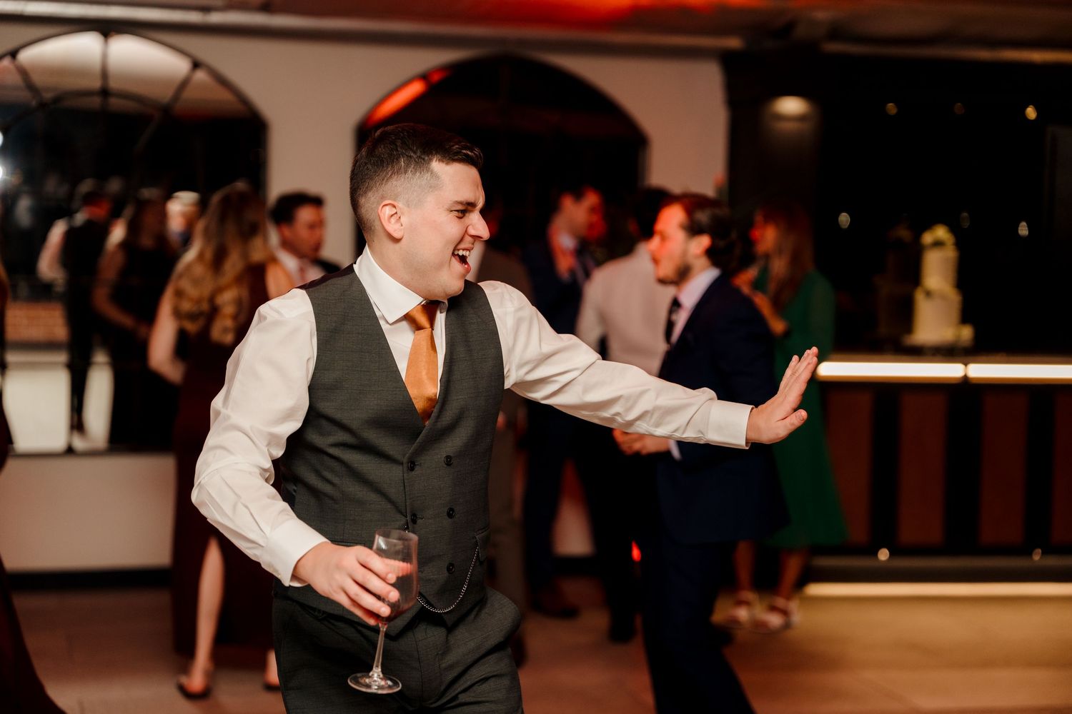 Energetic wedding guest in waistcoat and orange tie dancing at reception party.