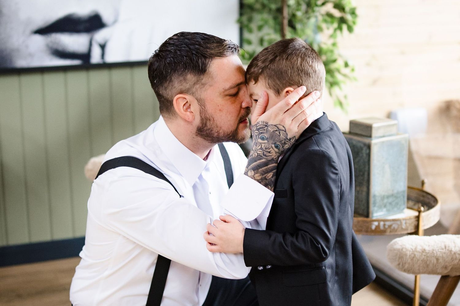 Two grooms sharing a kiss during their wedding ceremony, one wearing suspenders and the other in a black suit.