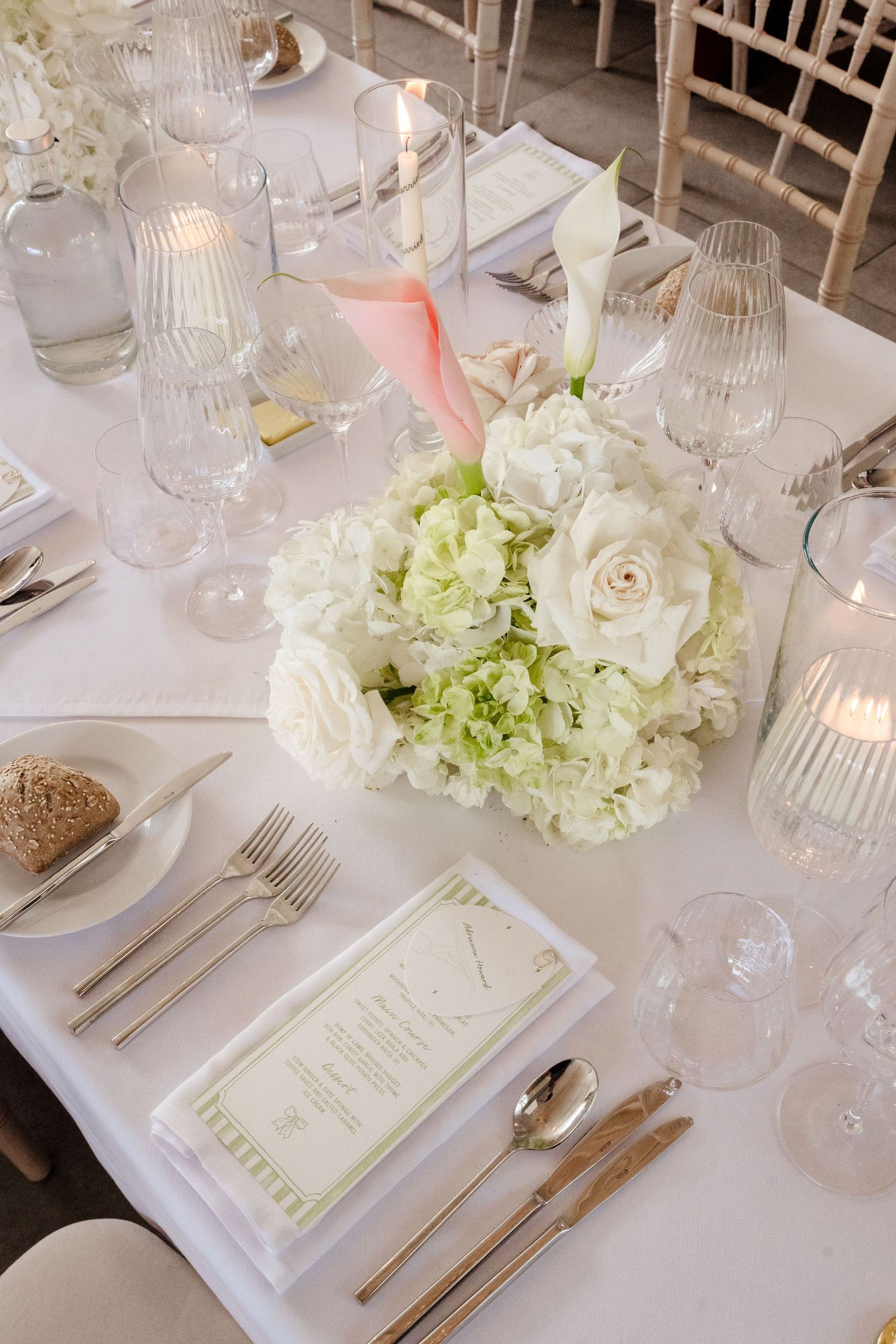 Elegant wedding table setting with white hydrangea centerpiece, candles, crystal glasses and menu cards.