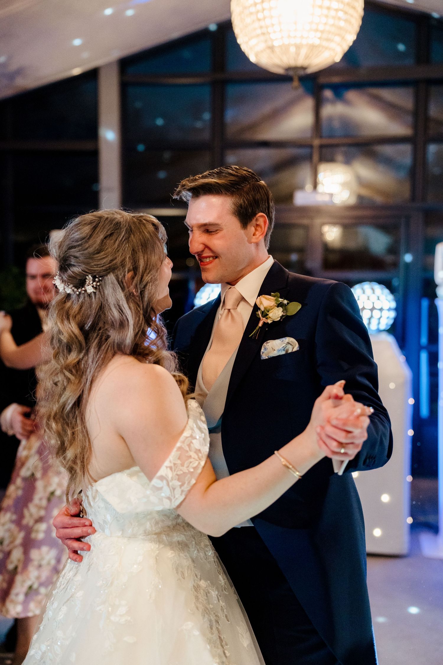 Bride and groom share their first dance at wedding reception under elegant chandelier lighting.