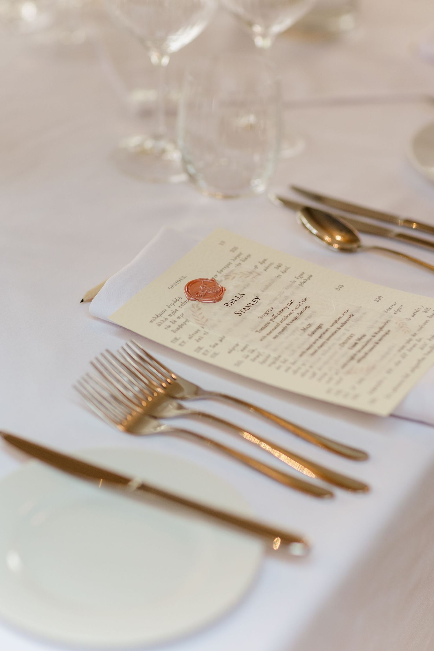 Elegant wedding table setting with gold cutlery, wax-sealed menu card, and crystal glasses.