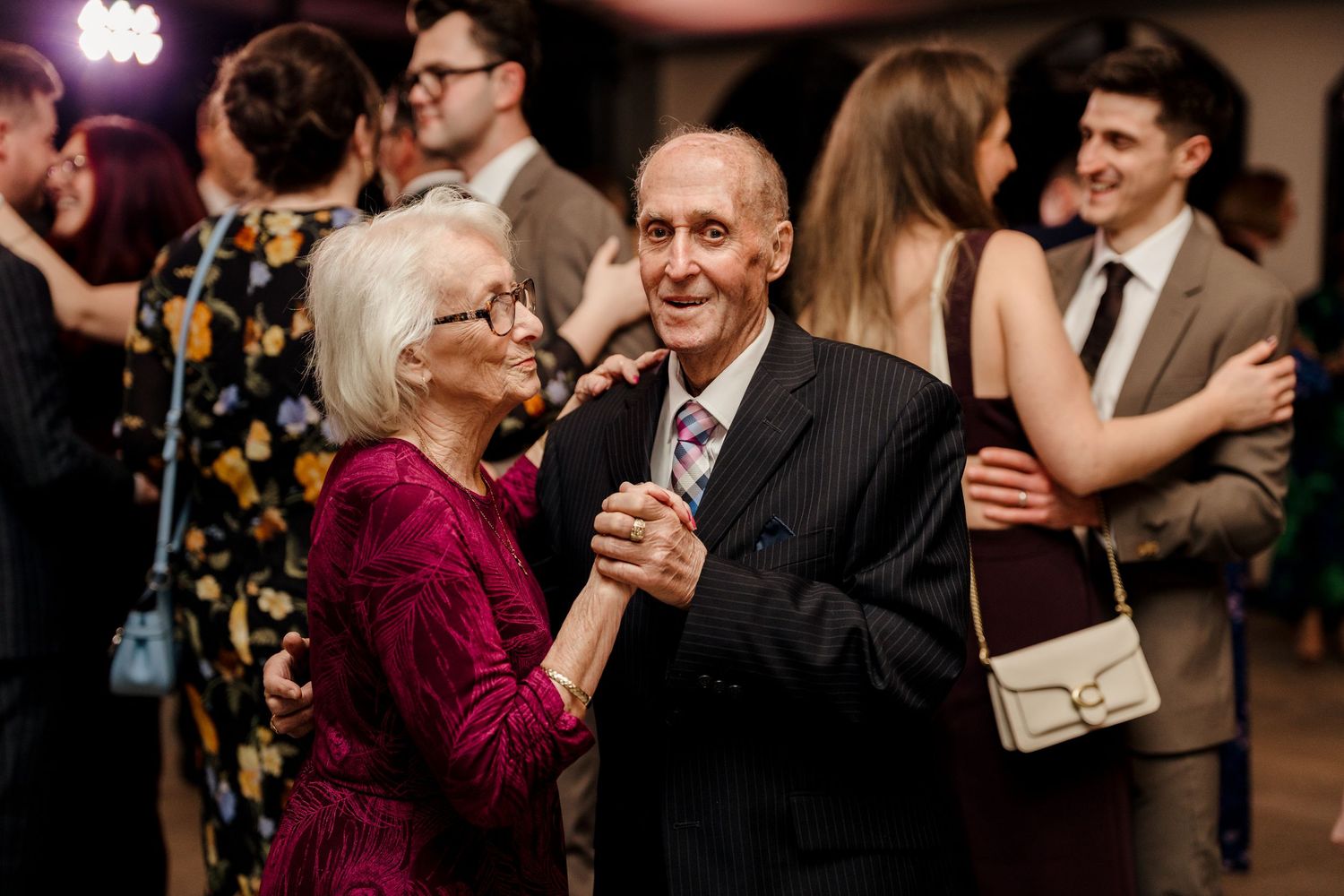 Elderly couple sharing a romantic dance together on the wedding reception dance floor surrounded by guests.