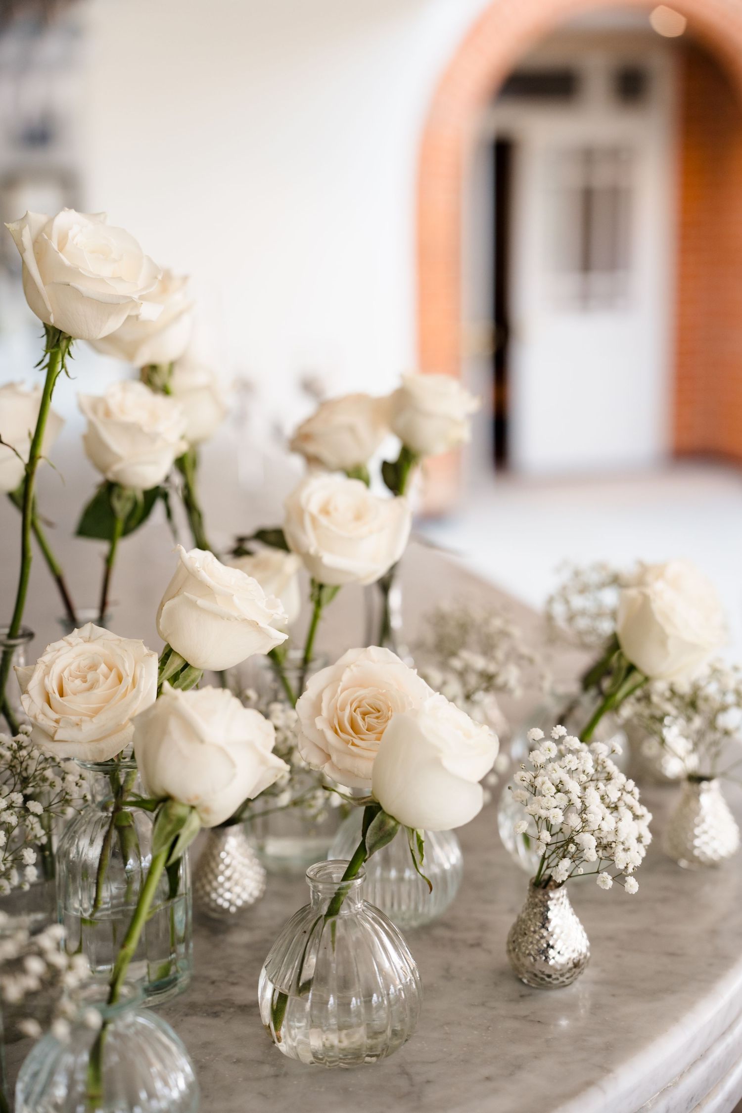 White roses and baby's breath arranged in small glass vases on a marble surface at a wedding reception.