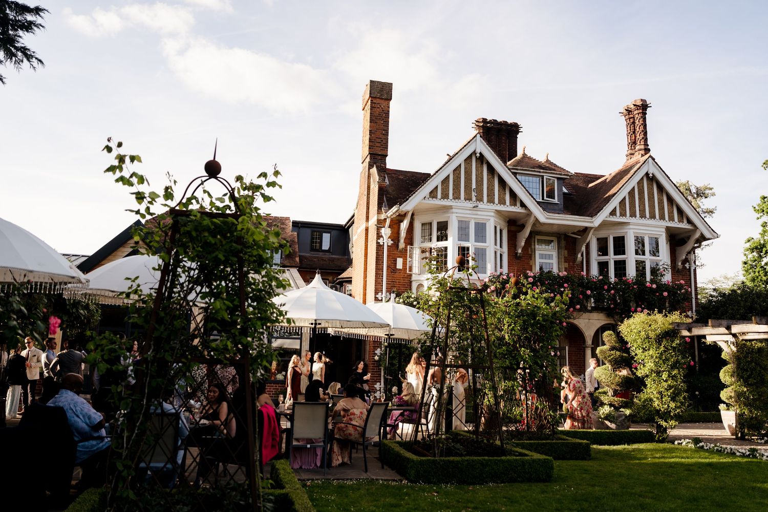 Guests mingle in the garden of a charming Tudor-style wedding venue during a summer evening reception.