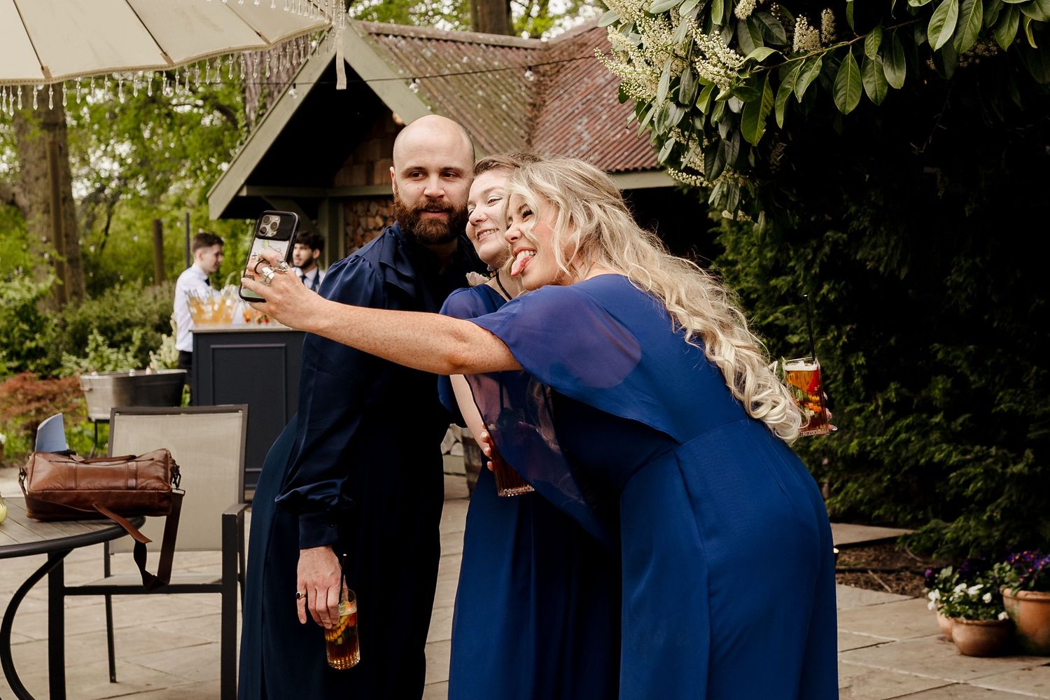 Bearded man and blonde woman in navy blue attire taking a selfie at an outdoor wedding reception.