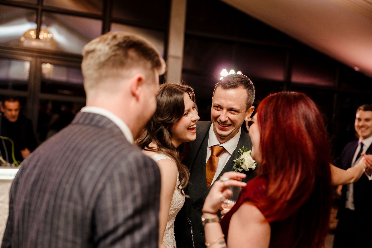Bride and groom smiling with guests during a lively wedding reception celebration.