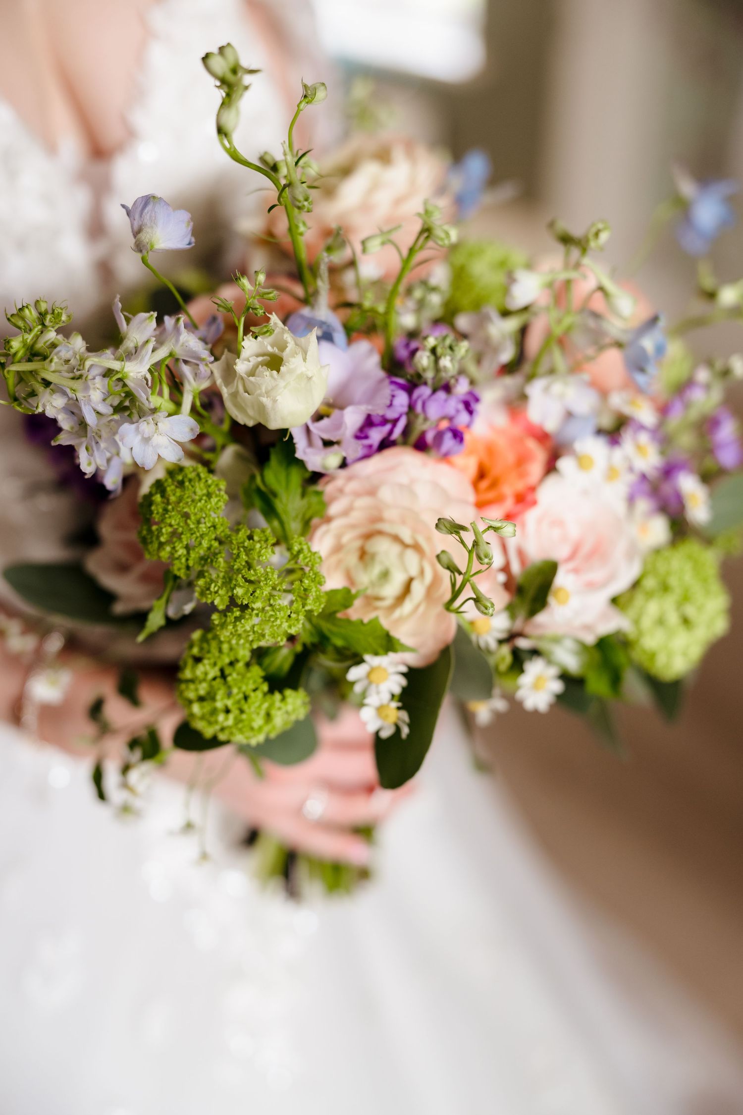 Bride holding a lush wedding bouquet with pink, purple, and green flowers in a white gown.