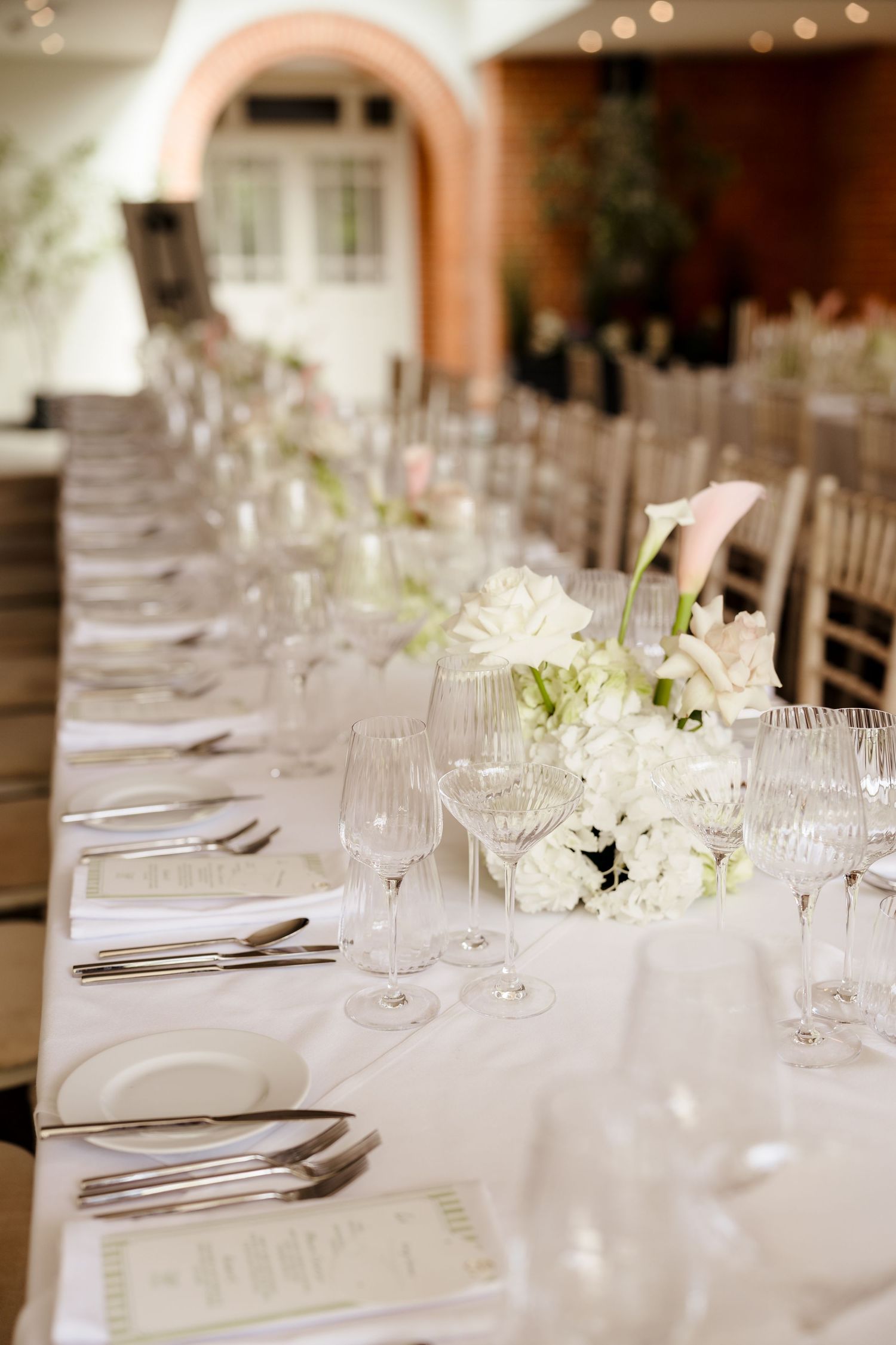 Elegant wedding reception table set with white floral centerpieces, crystal glasses and fine cutlery.