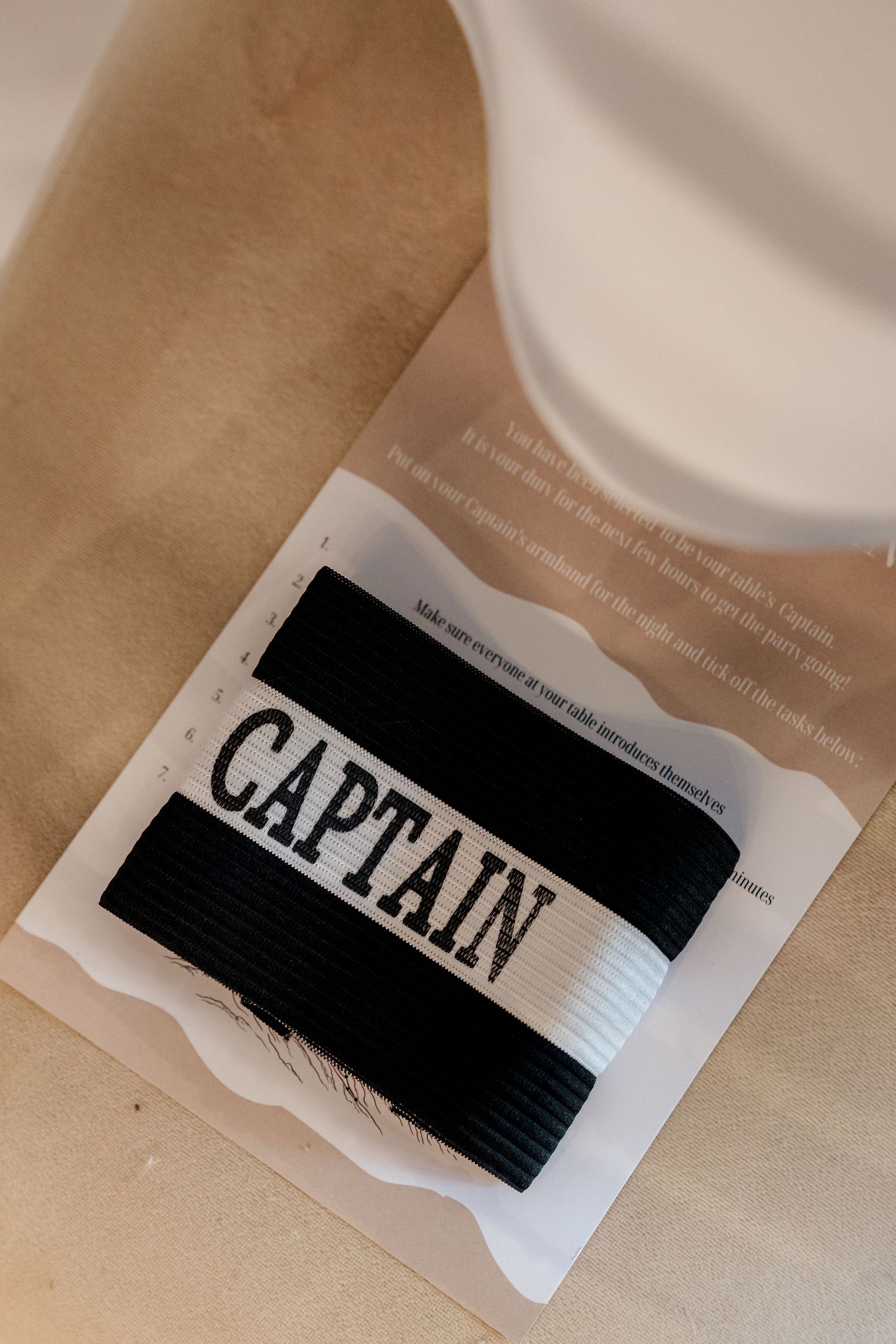 Black and white Captain armband displayed on kraft paper packaging for a fun wedding table game activity.