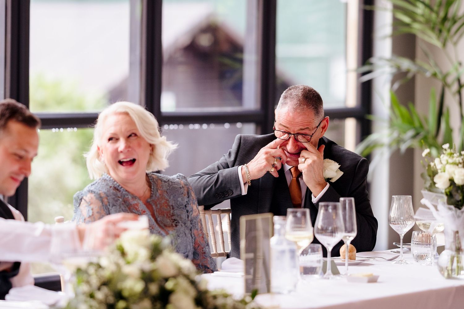 Joyful wedding guests laughing and crying with emotion during speeches at reception dinner table.