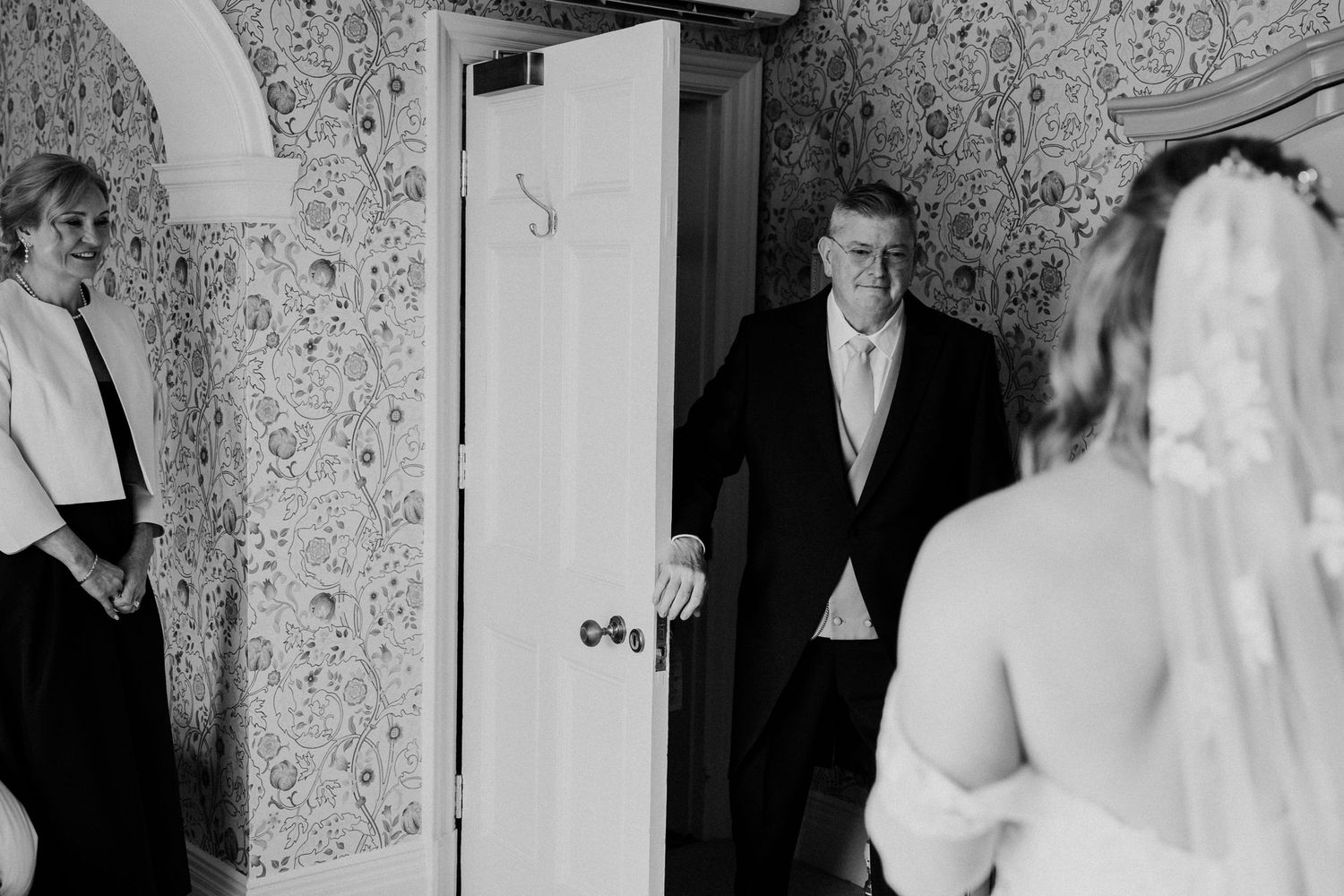 Black and white photo of a bride in veil seeing her father enter the room on her wedding day.