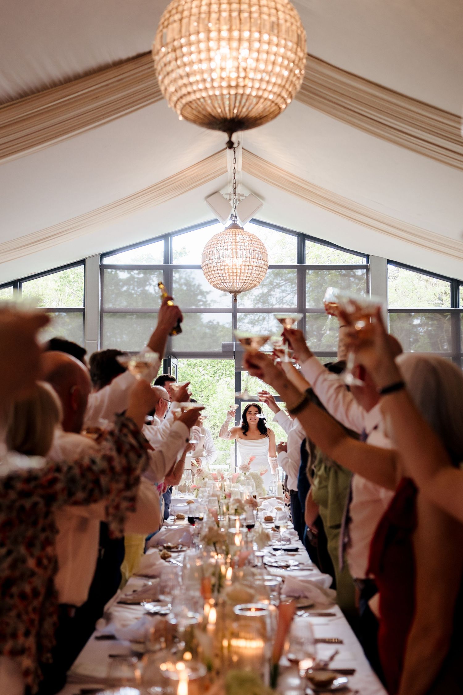 Bride walking between guests raising champagne glasses in stunning draped marquee wedding reception.