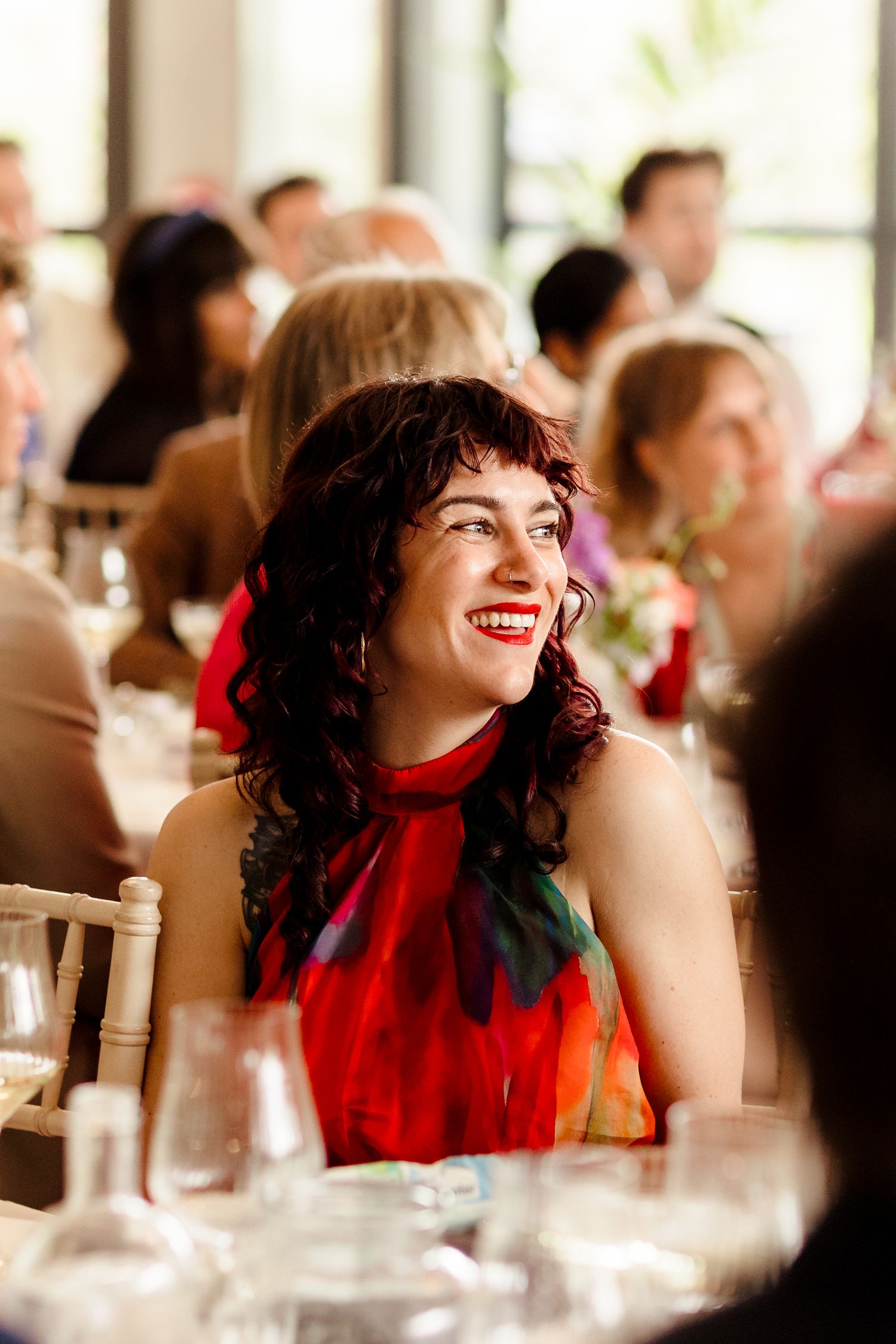Joyful female wedding guest in a vibrant red floral dress laughing during the reception.
