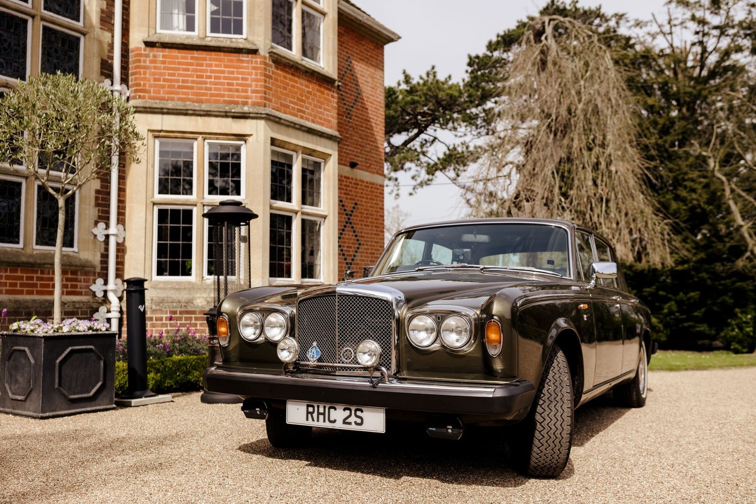 Vintage Bentley classic car with license plate RHC 25 parked on gravel driveway outside elegant brick manor house.