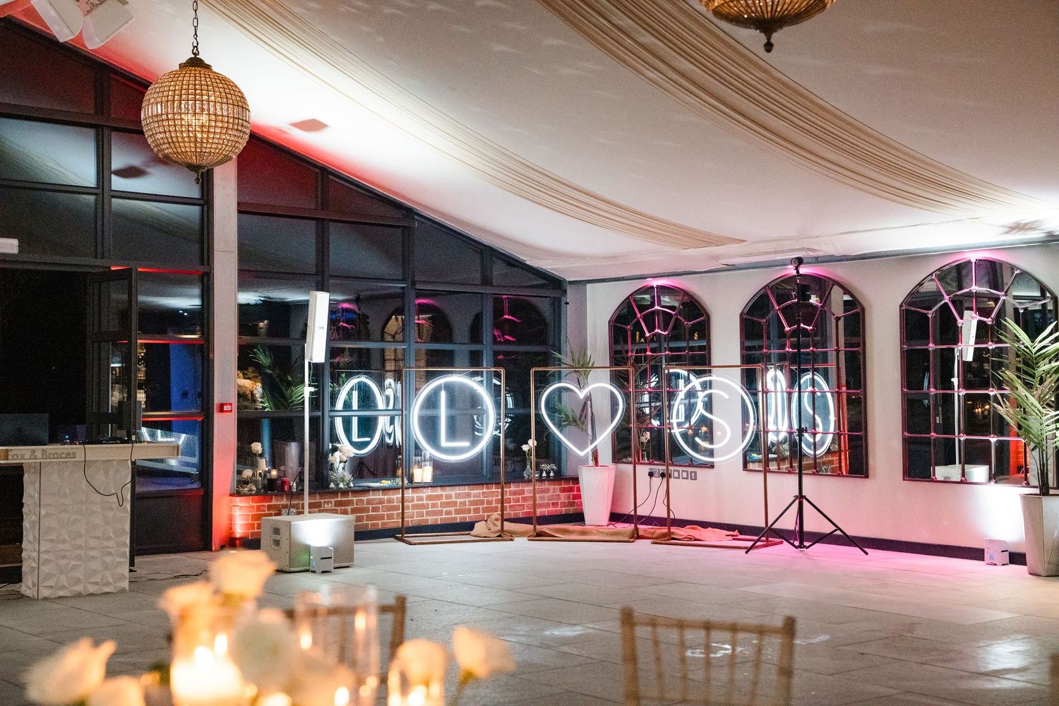 Wedding reception venue with neon light decorations spelling LOVE on dance floor with draped ceiling.