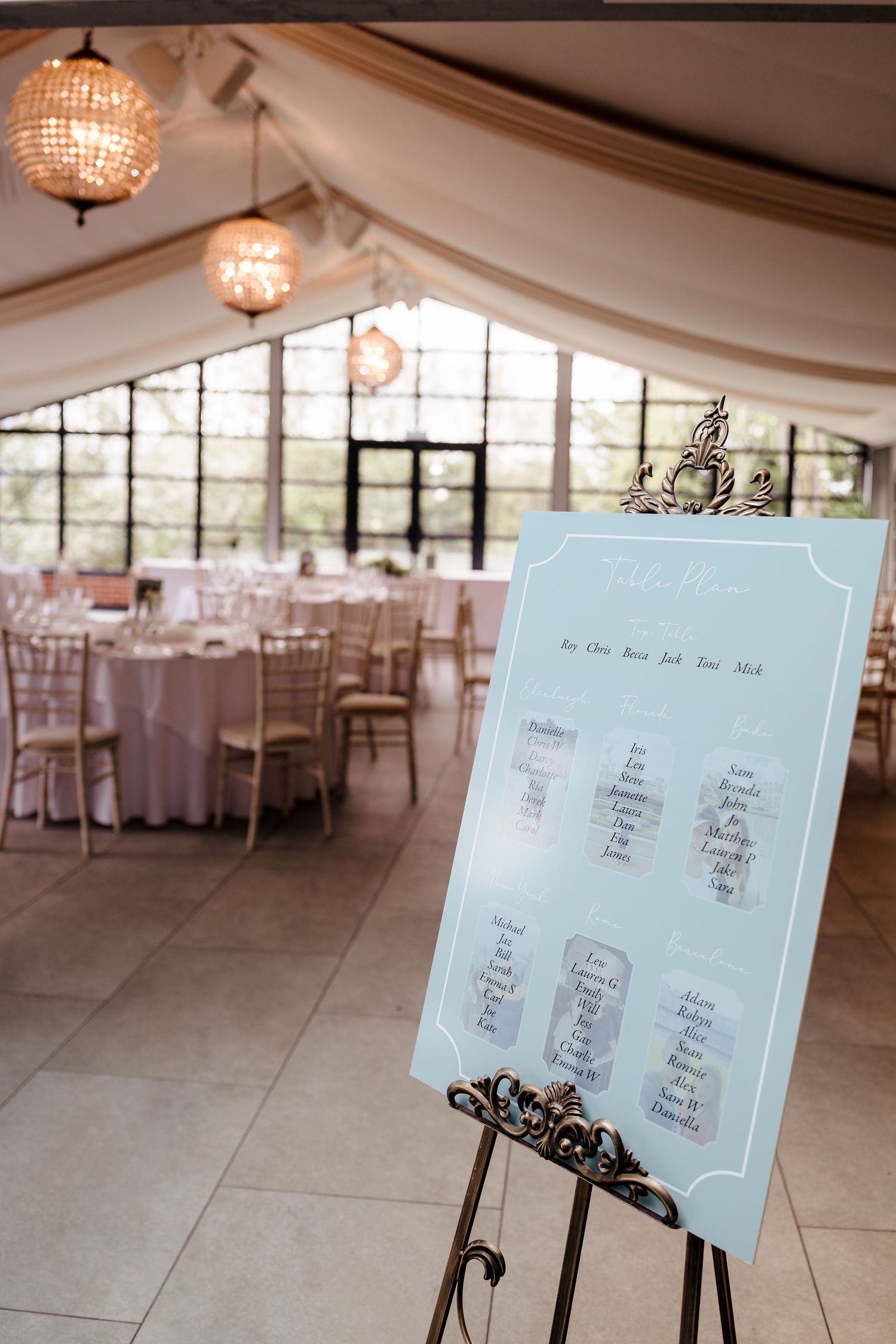 Elegant wedding reception seating chart on easel in beautifully decorated venue with chandelier lighting.