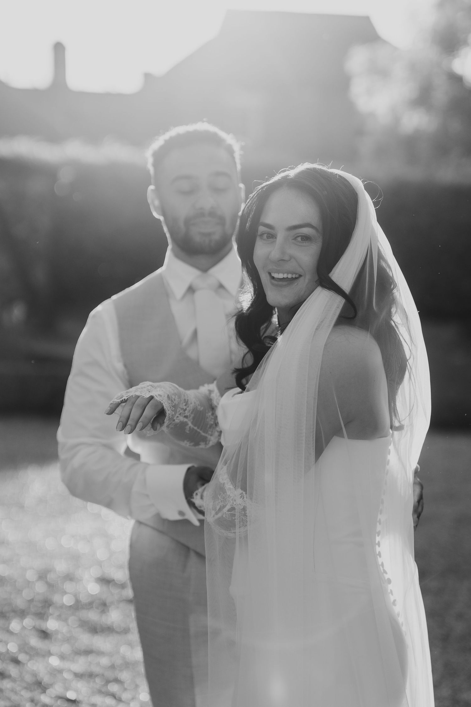 Black and white portrait of a smiling bride and groom embracing in golden backlit sunlight.