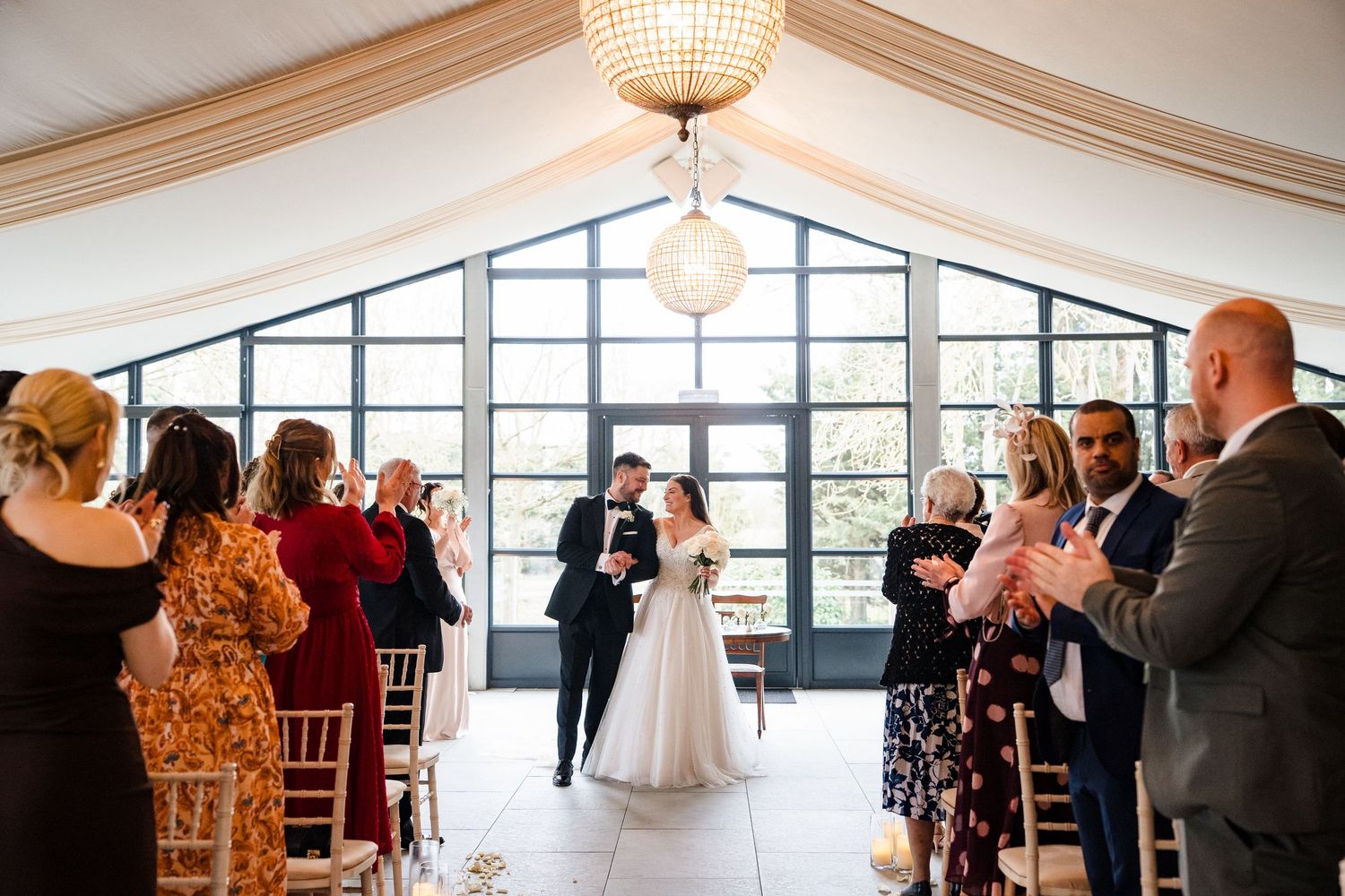 Bride and groom walk down the aisle at elegant wedding ceremony venue with guests applauding.