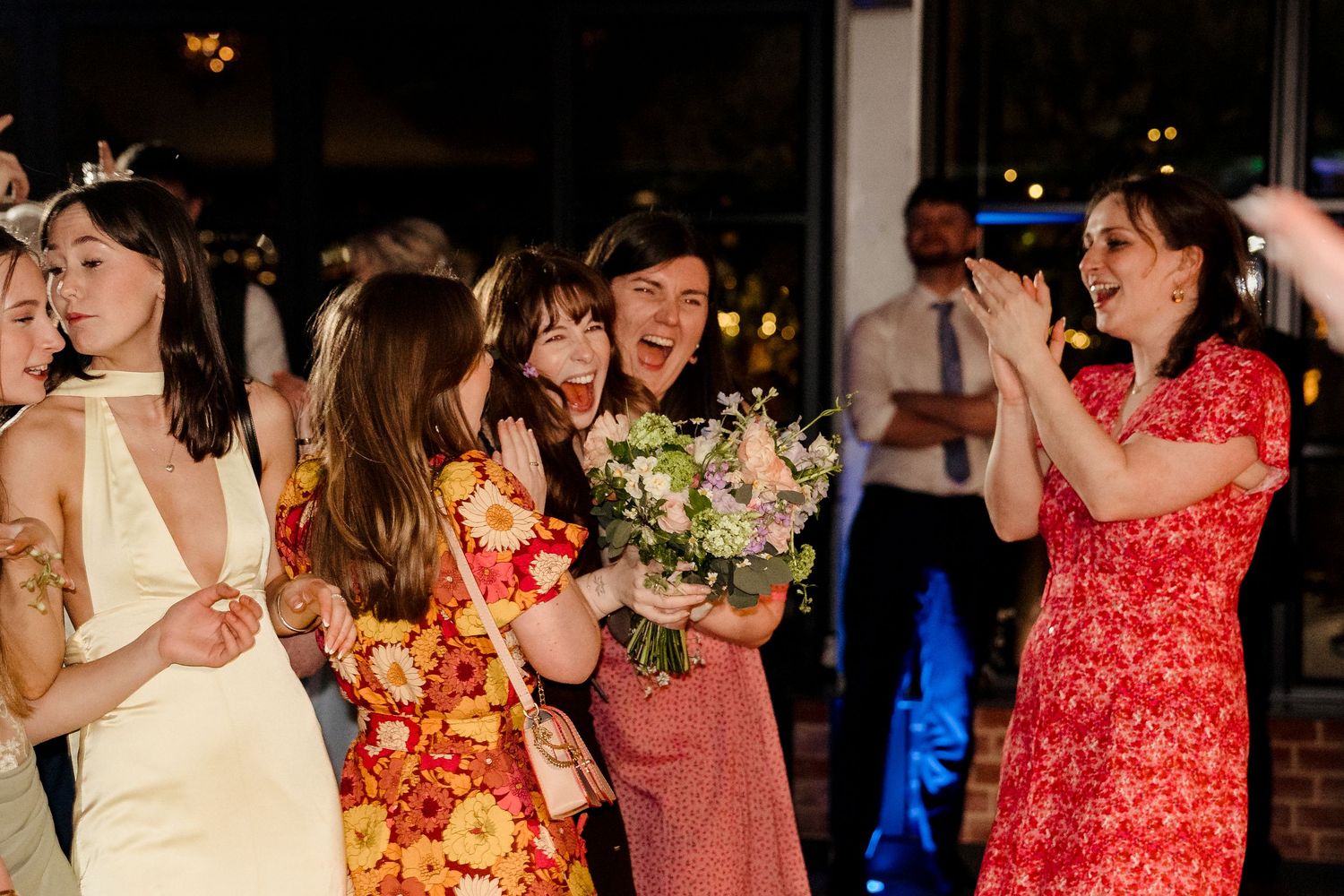 Happy wedding guests celebrating as one woman catches the bridal bouquet at the reception.