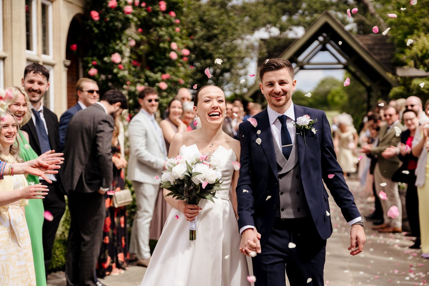 Joyful newlyweds walk through confetti shower surrounded by cheering guests outside a charming venue on their wedding day.