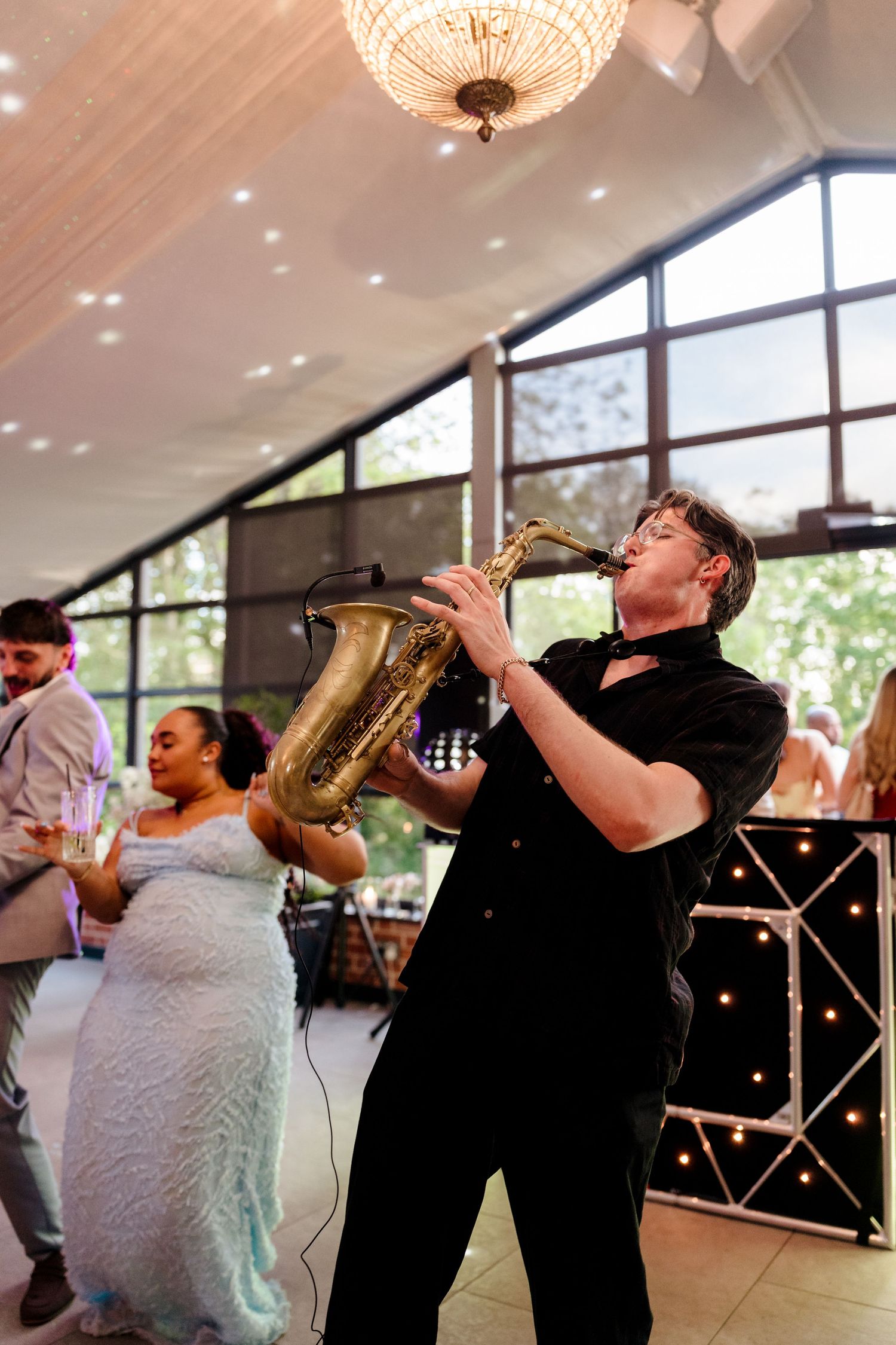 Saxophonist performs energetically on the dance floor at a wedding reception while guests celebrate behind him.