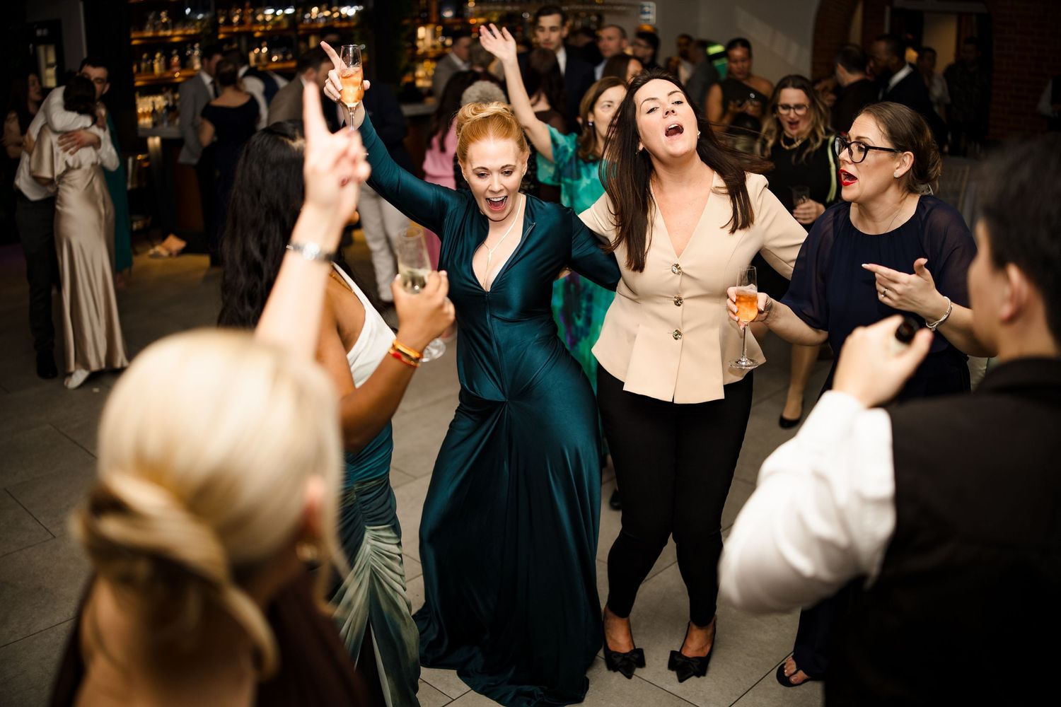 Wedding guests in formal attire dancing and celebrating joyfully on the dance floor at a lively reception.