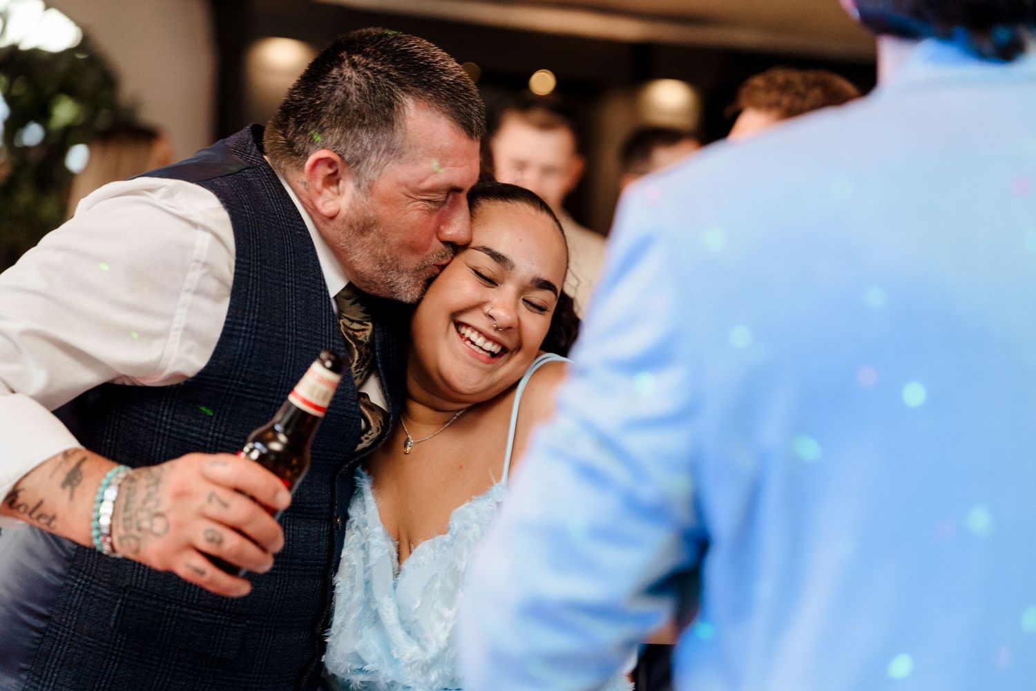 Older man kissing laughing bride on cheek at wedding celebration.
