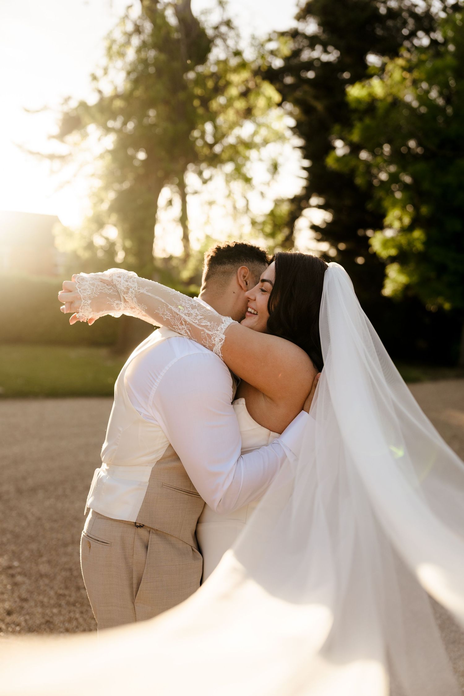 Bride and groom sharing romantic kiss in golden hour sunlight with flowing veil.