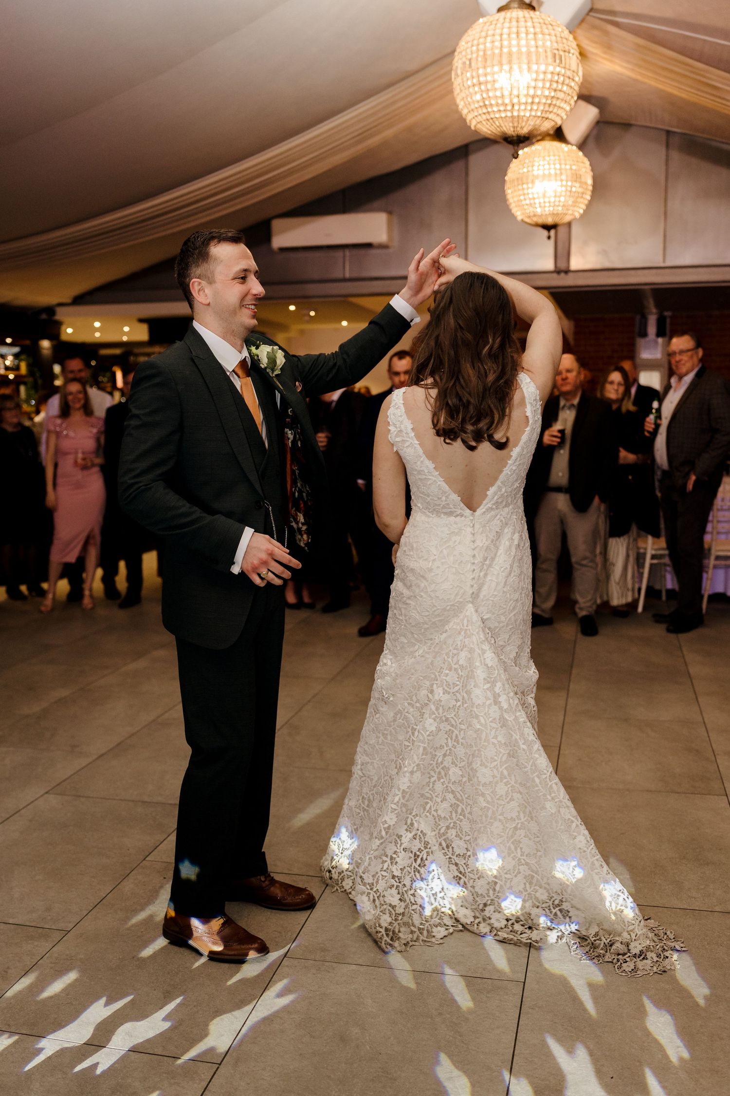 Groom spinning bride in lace wedding dress during their first dance at the reception.