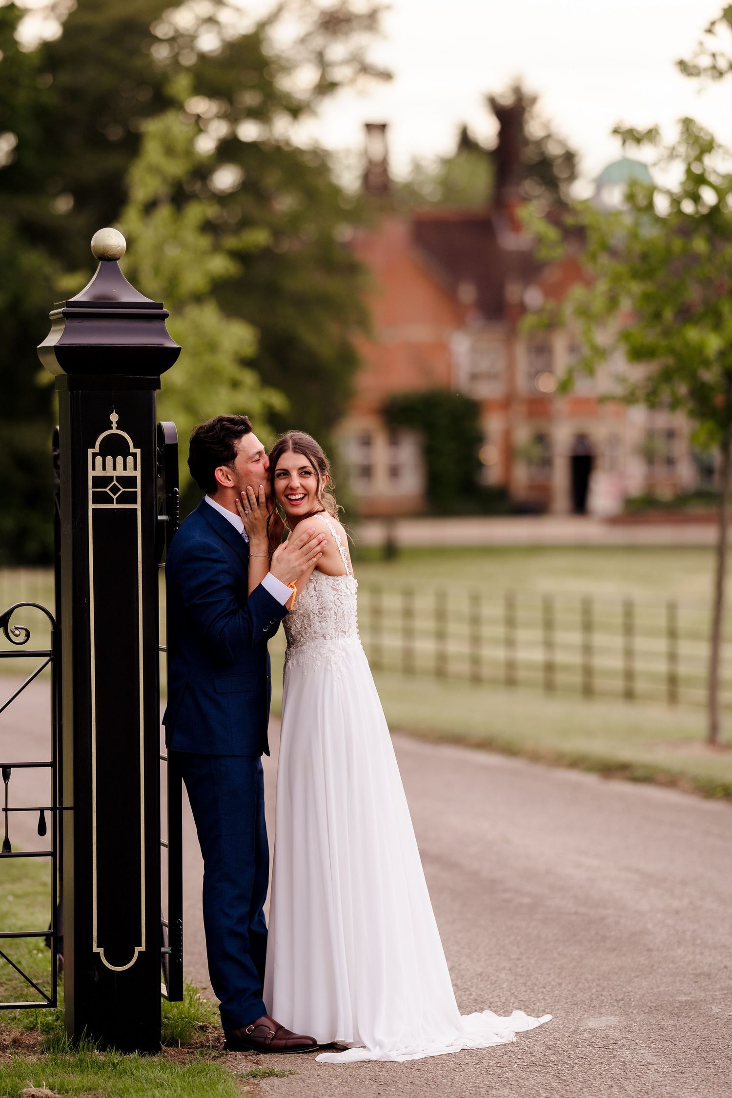 Bride and groom share a romantic moment by ornate gate at elegant manor house wedding venue.