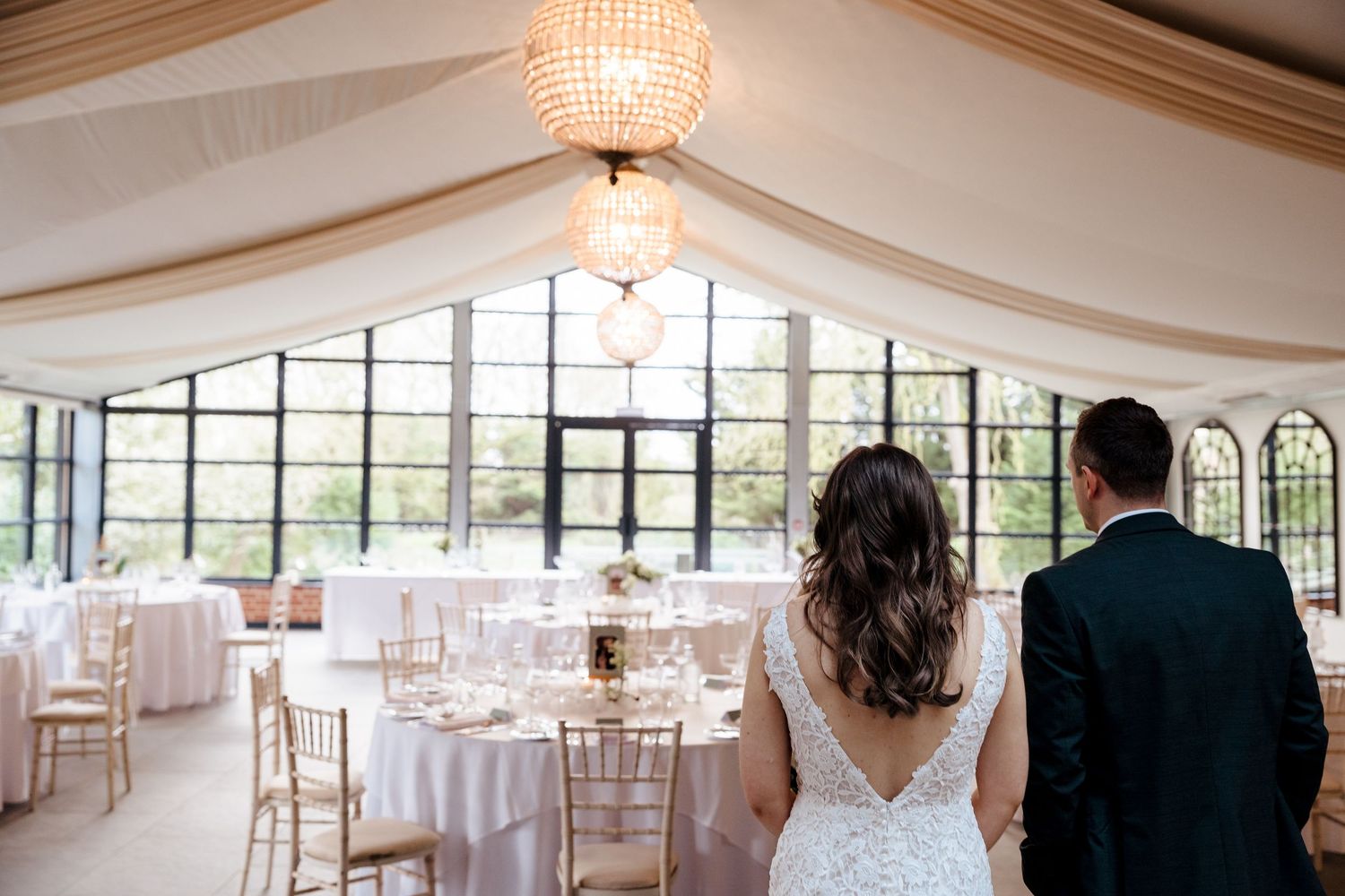 Bride and groom entering an elegant white draped wedding reception venue with chandeliers.