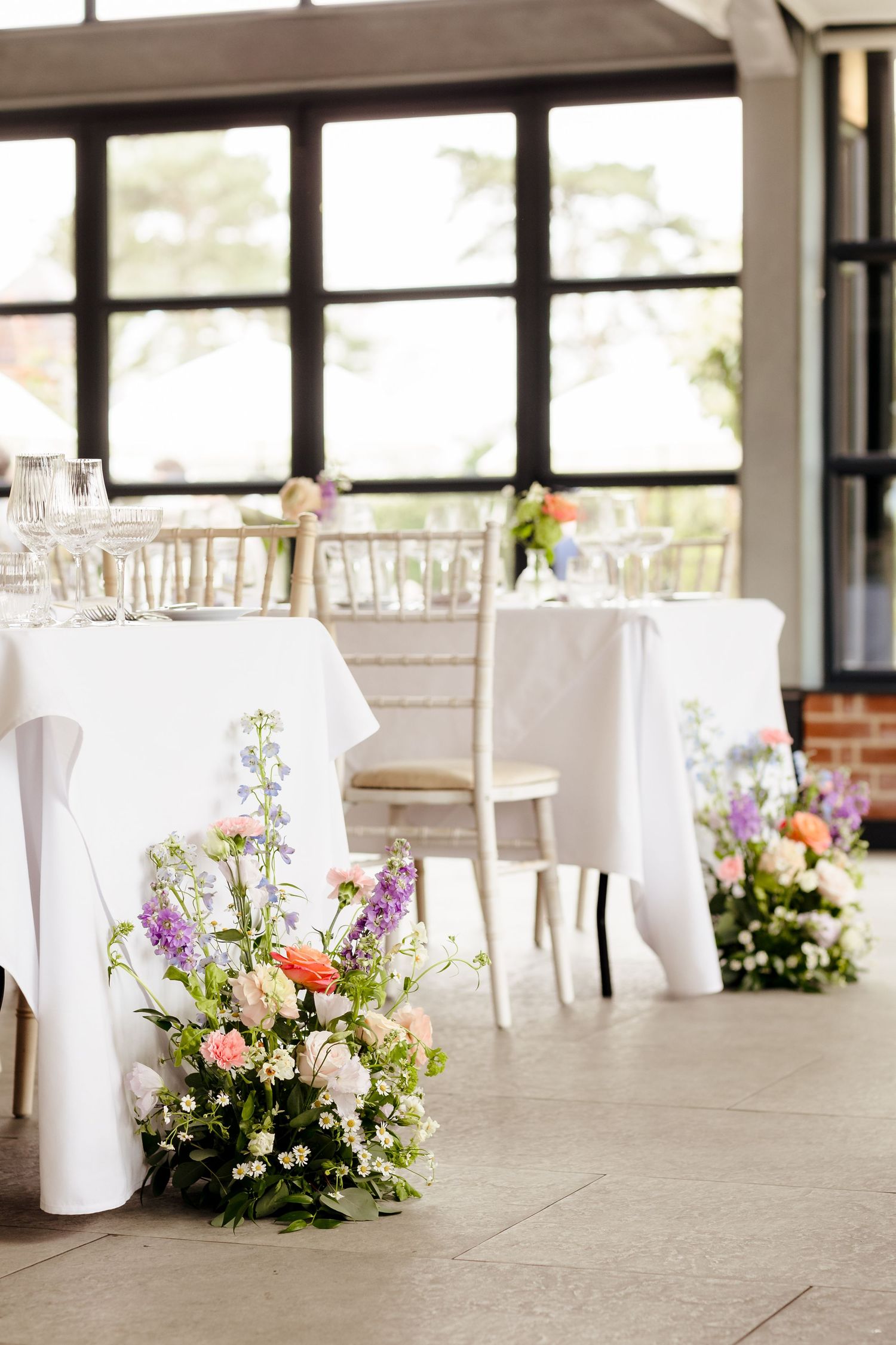 Elegant wedding reception venue with white tablecloths, chiavari chairs, and colorful floral arrangements on the floor.