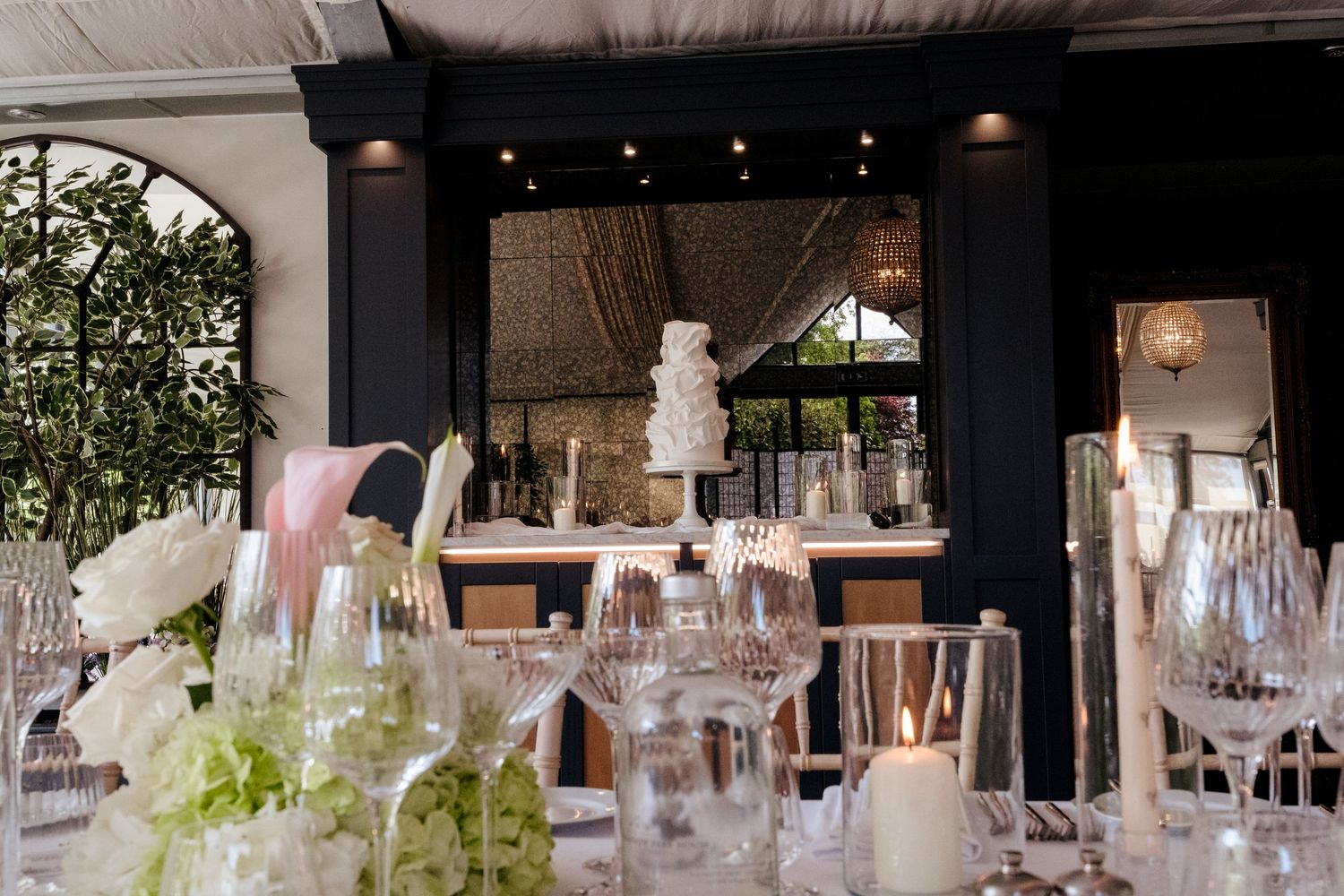Elegant wedding reception table with white cake, crystal glasses, and floral decor.