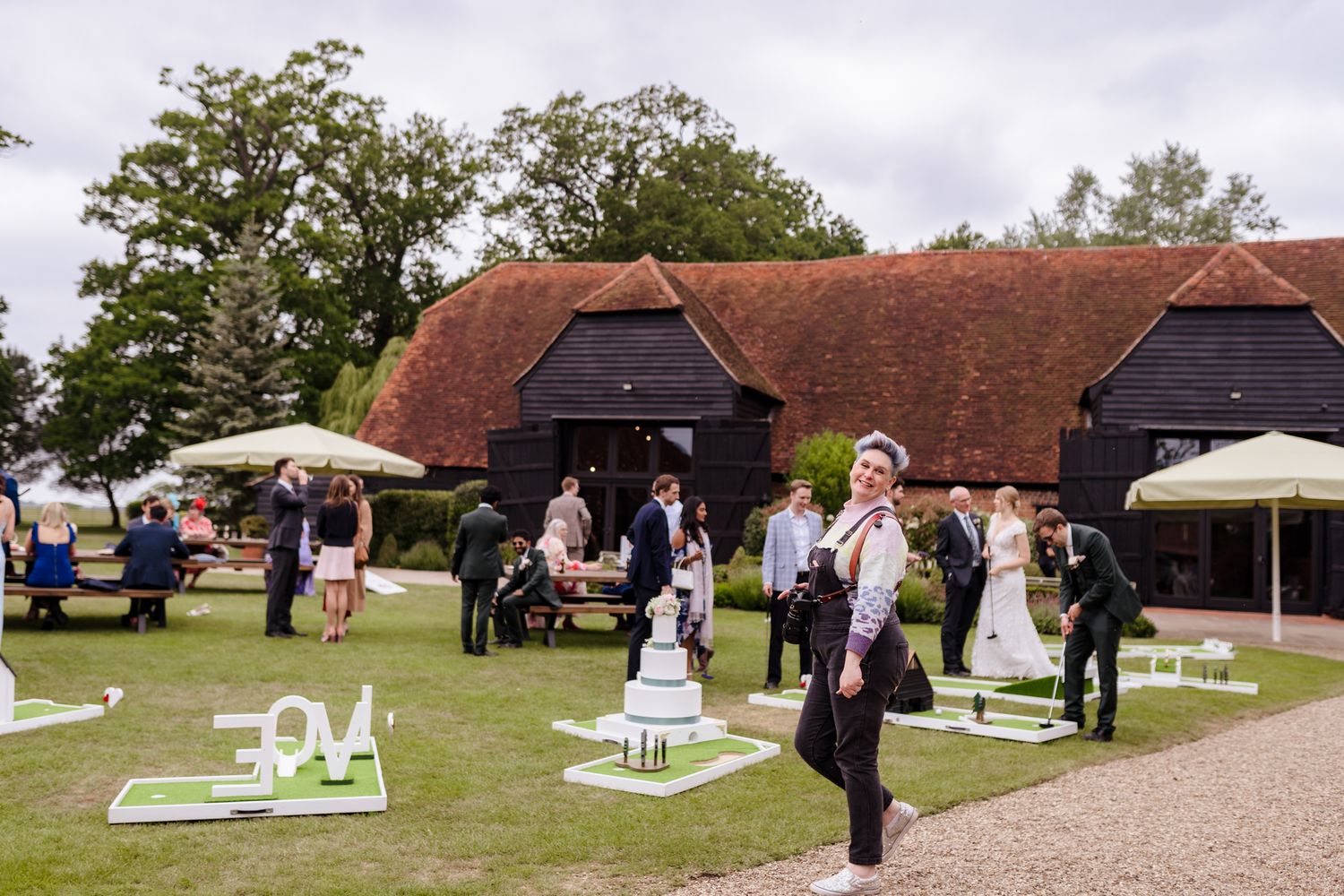 Outdoor wedding reception at a rustic barn venue with guests mingling on manicured lawns with decorative displays.