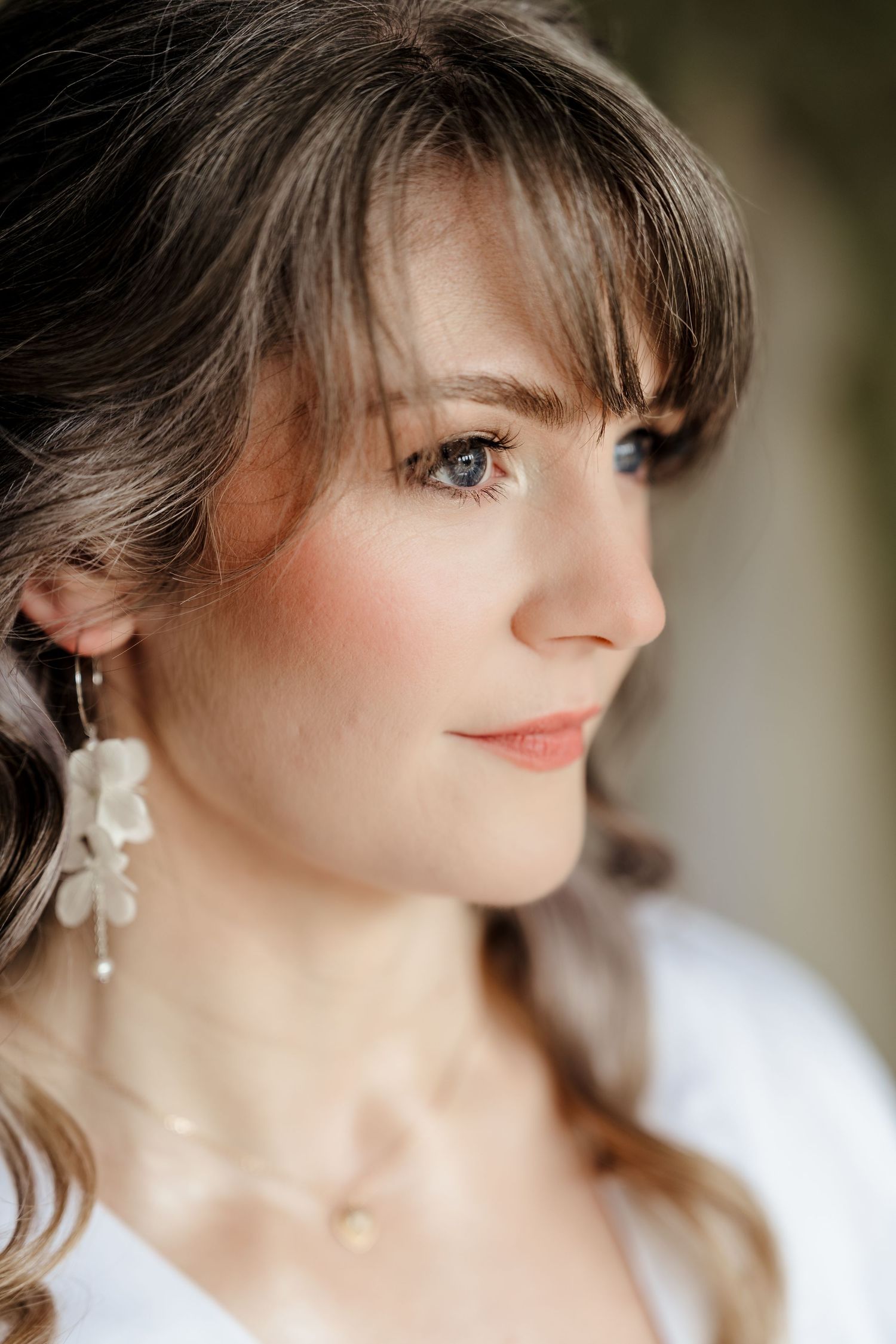 Close-up portrait of a bride with blue eyes wearing floral drop earrings and delicate gold necklace on wedding day.
