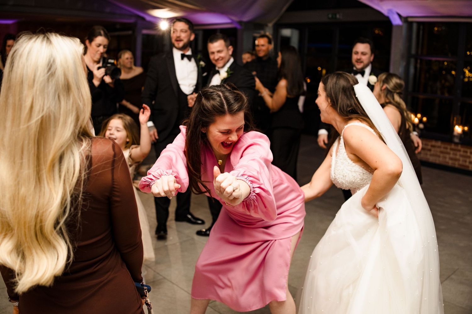 Bride and guests dance energetically together on the wedding reception dance floor at night.