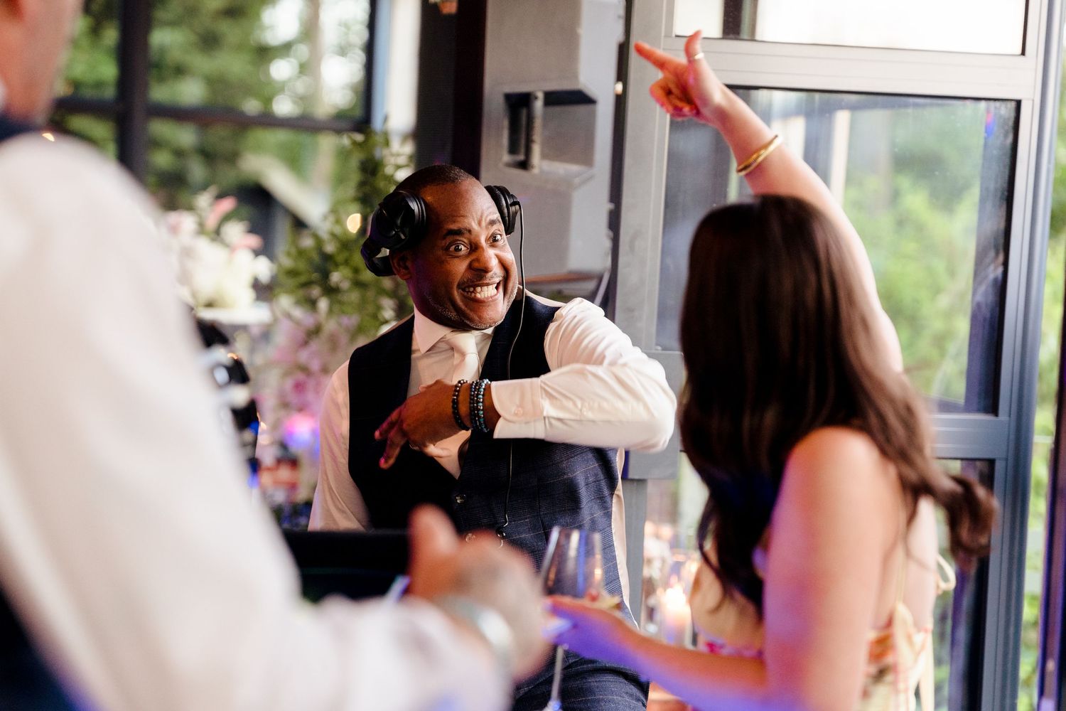Energetic DJ with headphones dances with wedding guests during lively indoor wedding reception celebration.