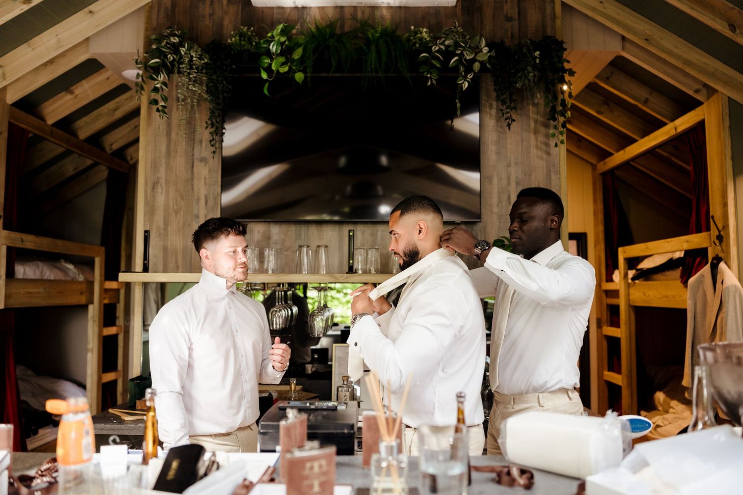 Groomsmen helping each other get dressed in a rustic barn venue before a wedding ceremony.