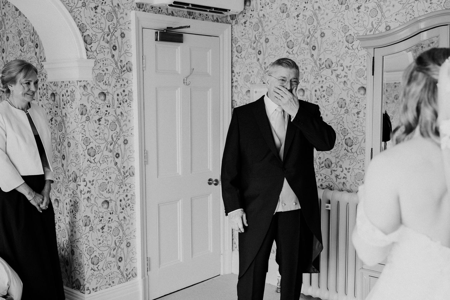 Emotional groom covering his mouth as he sees bride for first time, black and white wedding photo.