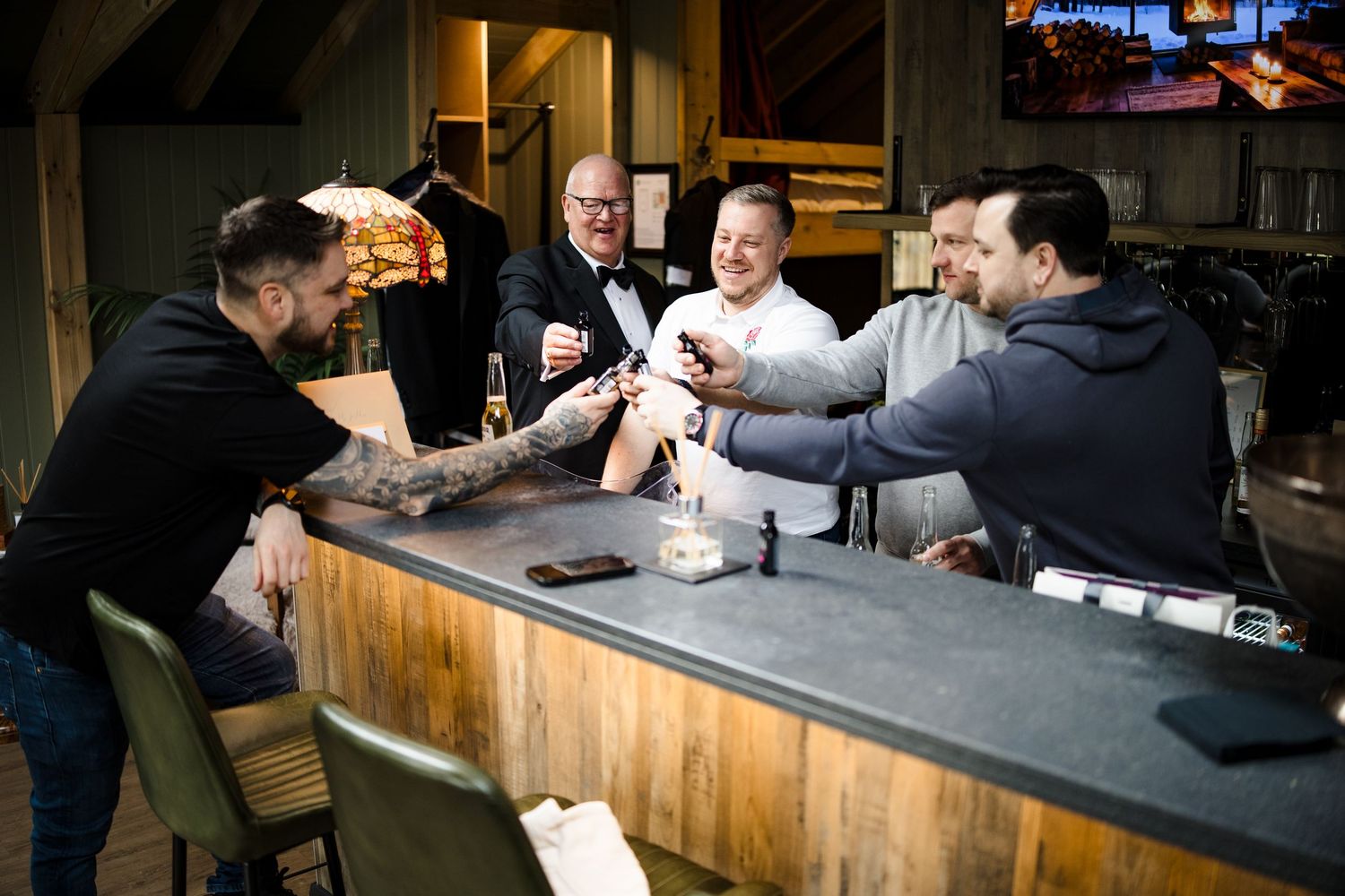 Five men gathered around a rustic wooden bar, socializing and sharing drinks in a cozy restaurant setting.