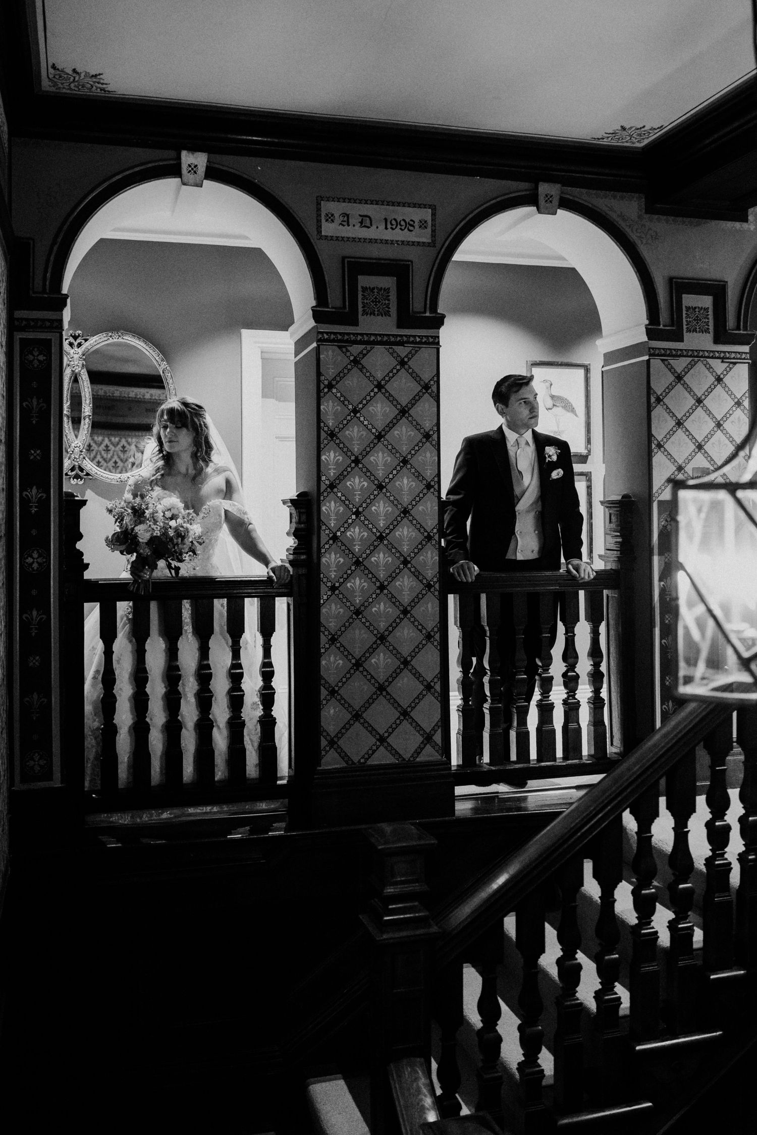 Black and white photo of bride and groom standing on a grand staircase balcony at a historic wedding venue.