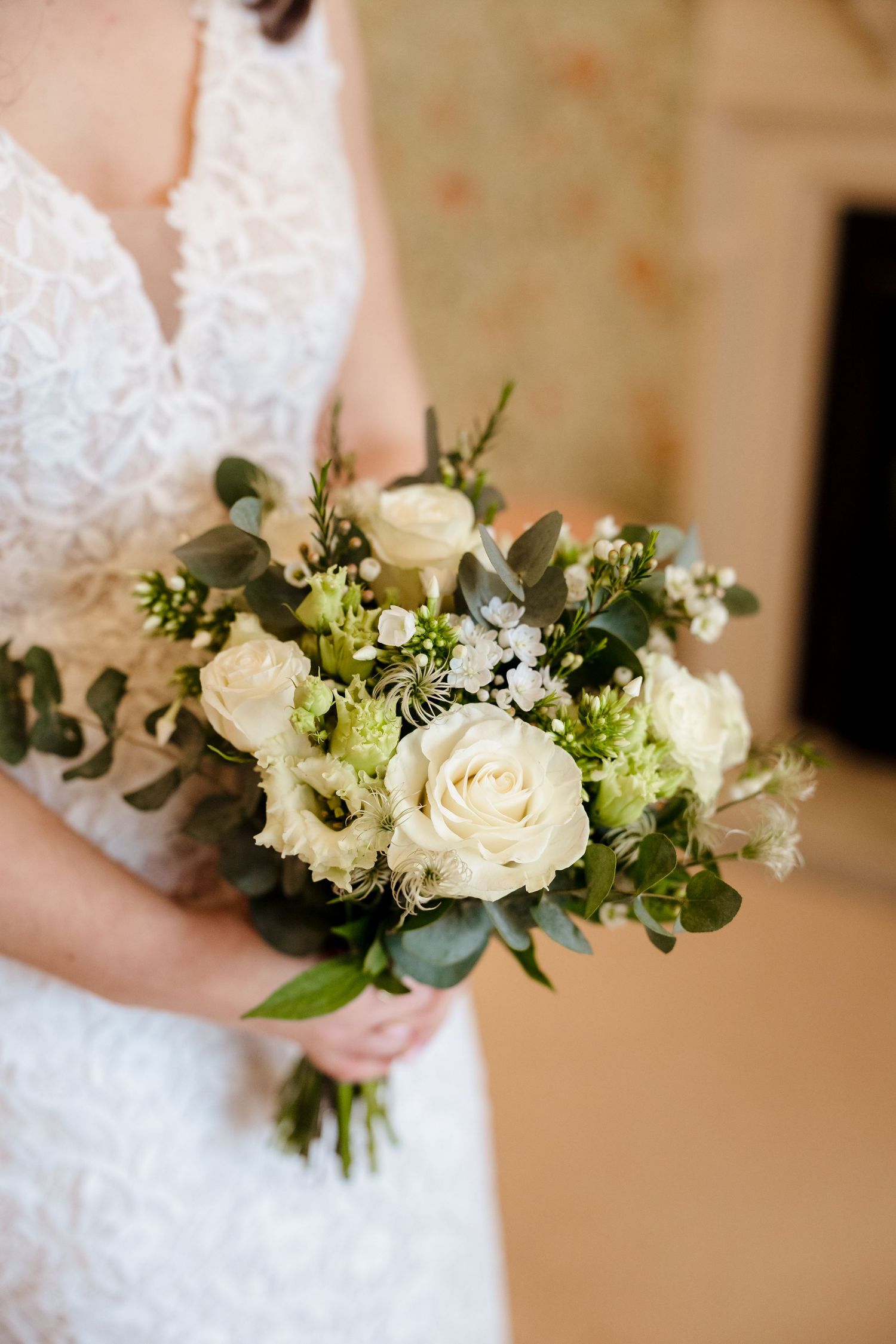 Bride holding an elegant white rose and greenery wedding bouquet in a lace dress.