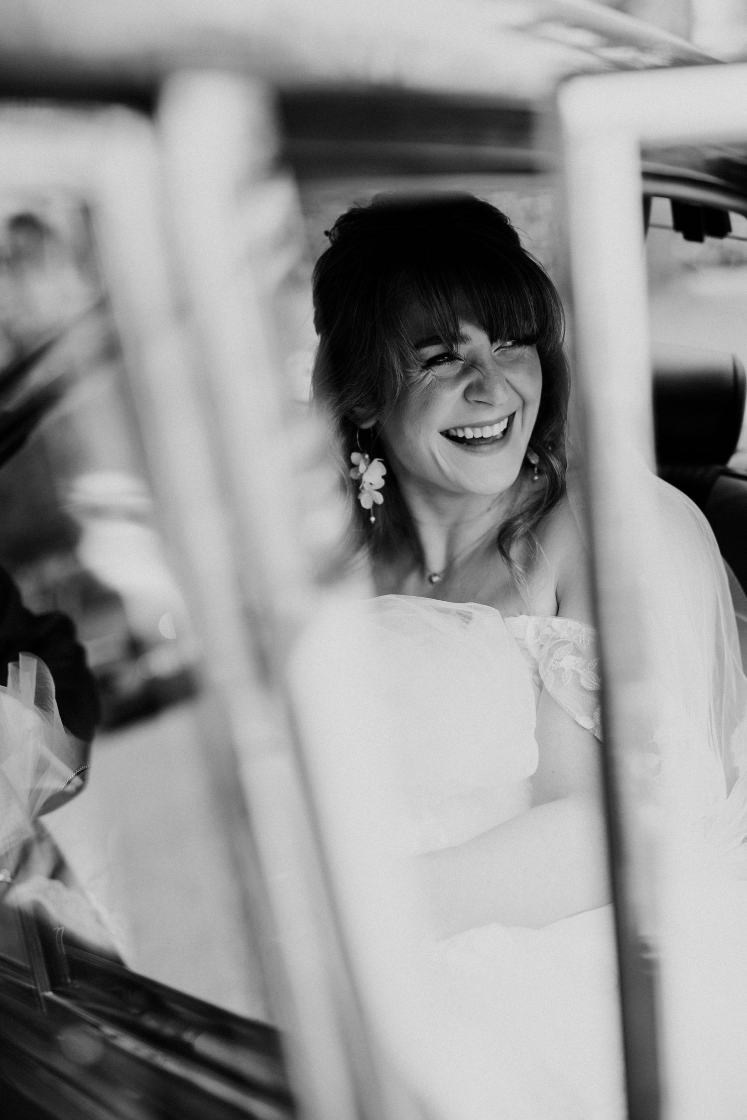 Joyful bride laughing in black and white portrait captured through window of wedding car.