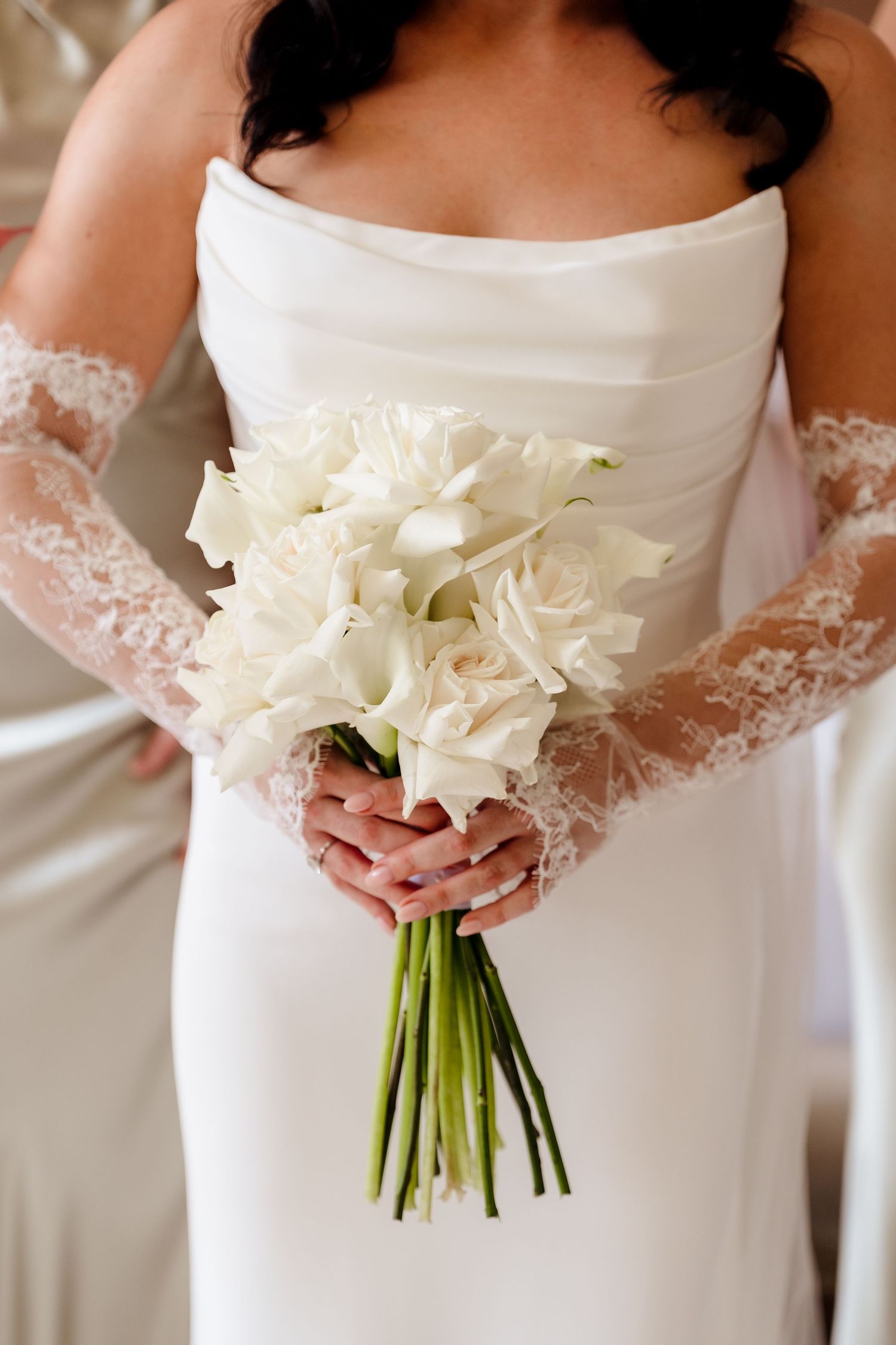 Bride in a white strapless gown holding an elegant bouquet of white calla lilies and roses.